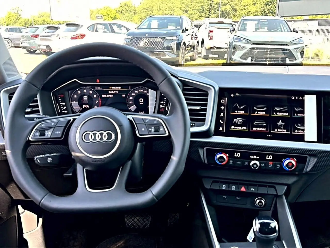 Vue intérieure centrée sur le volant multifonction et l'écran tactile du tableau de bord de l'Audi A1 Sportback noir.