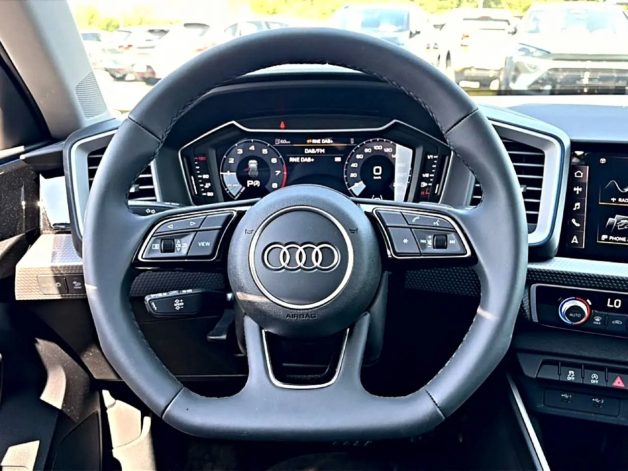 Vue frontale du volant cuir noir multifonction de l'Audi A1 Sportback avec tableau de bord digital et écran tactile.