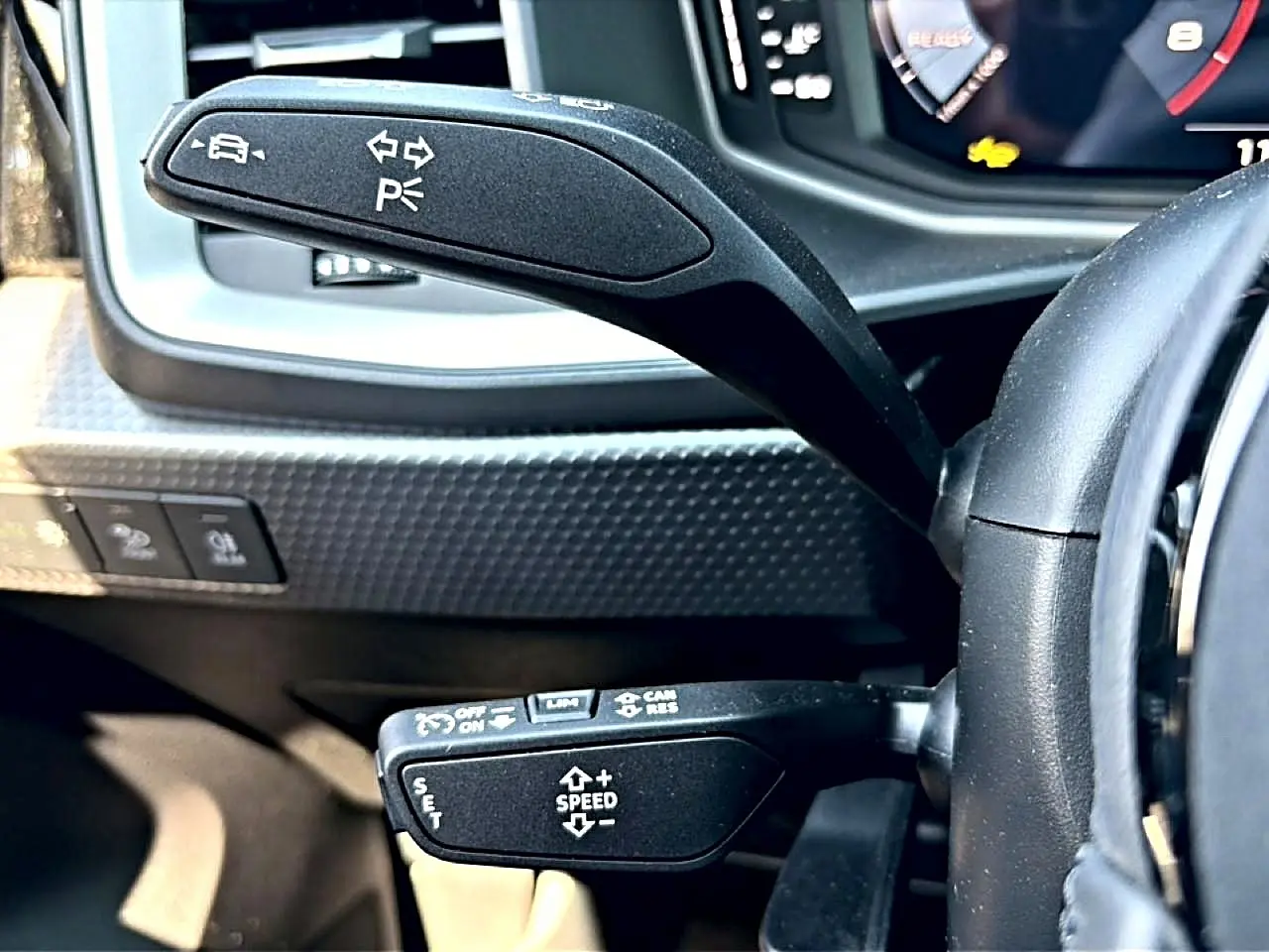 Gros plan sur les commandes au volant noir de l'Audi A1 Sportback 30 TFSI, avec tableau de bord numérique en arrière-plan.
