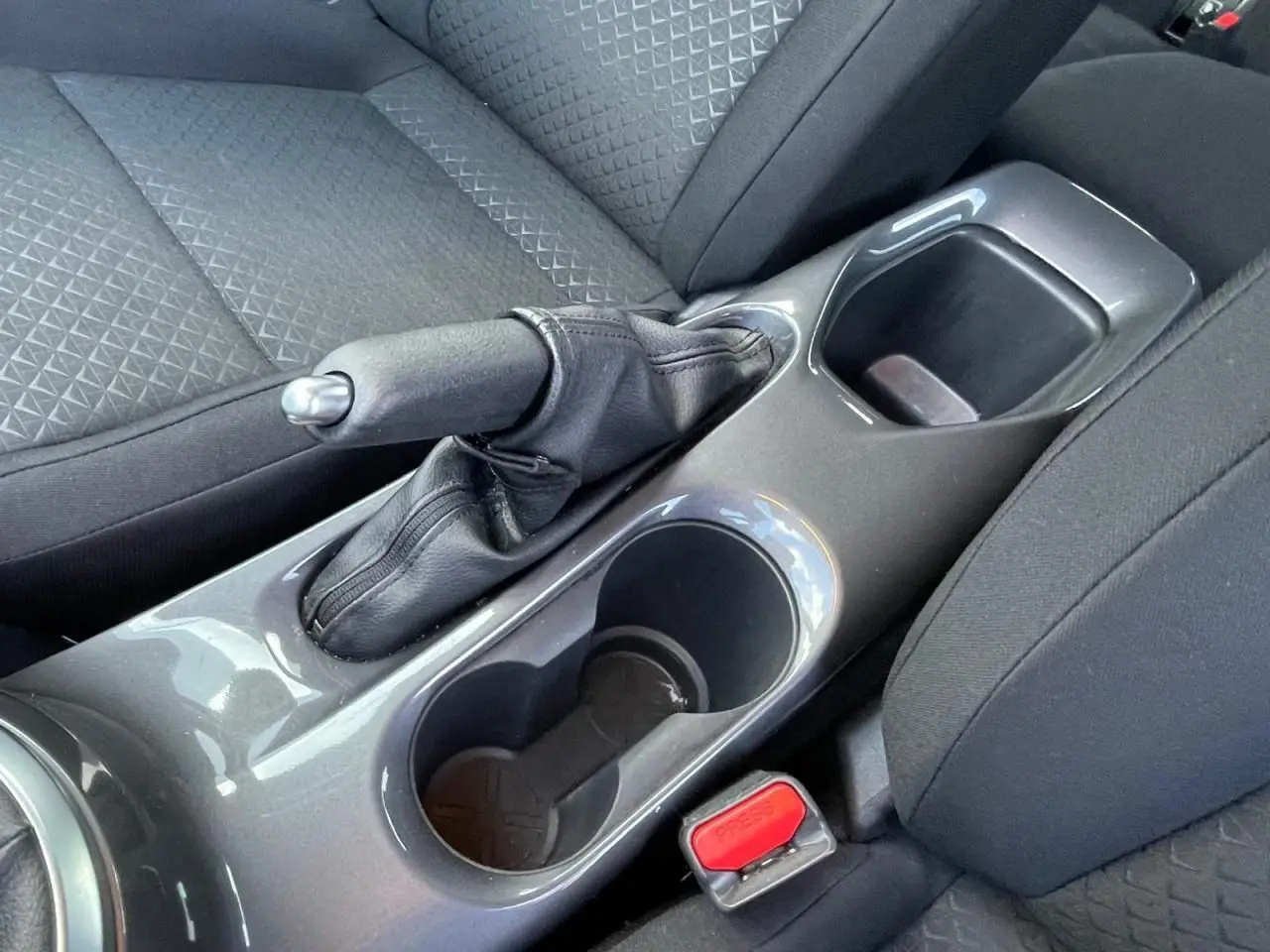 Gros plan sur la console centrale grise du Nissan Juke 2024, montrant frein à main manuel et porte-gobelets noirs.