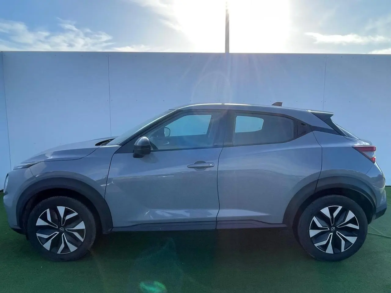 Profil côté gauche du Nissan Juke II gris ceramic 2024 avec jantes alliage noires et coques de rétroviseurs assorties.