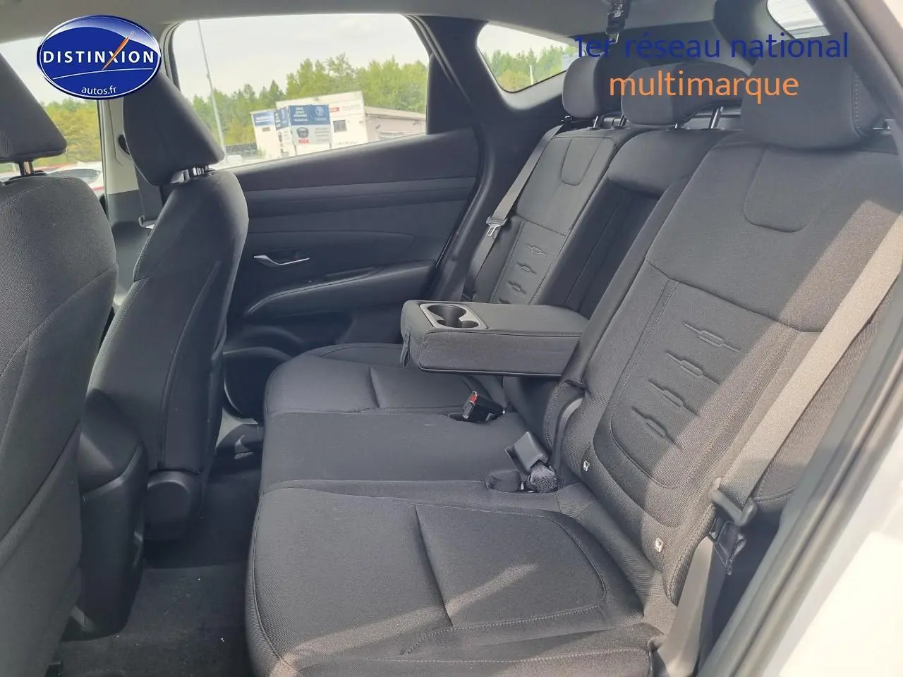 Vue intérieure côté droit des sièges arrière noirs avec accoudoir central déployé du Hyundai Tucson blanc atlas 2025.