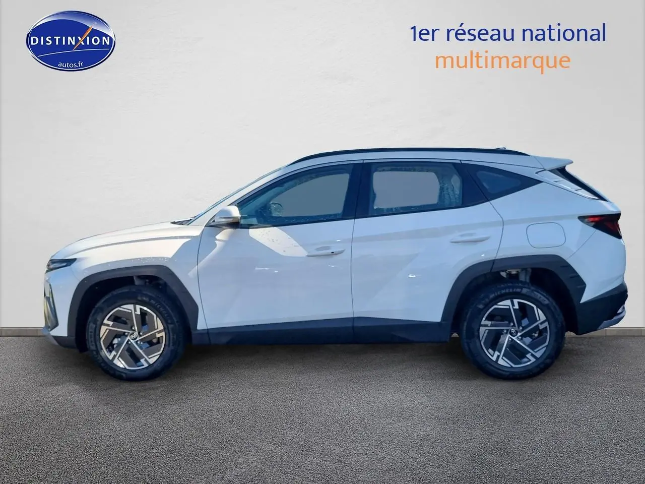 Profil côté gauche du Hyundai Tucson blanc atlas 2025 avec jantes alliage et barres de toit noires.
