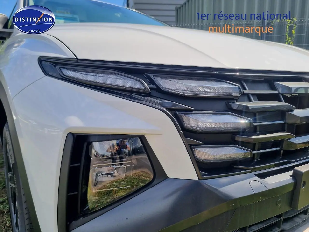 Gros plan sur l'avant droit du Hyundai Tucson blanc atlas 2025 avec calandre grise et feux LED distinctifs.