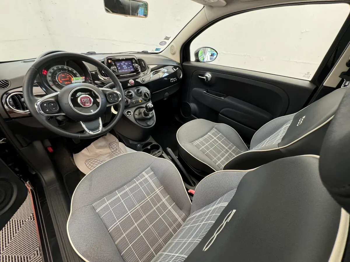 Vue intérieure avant droite de la FIAT 500 noire 2019, montrant le volant cuir, tableau de bord et sièges gris à motifs.