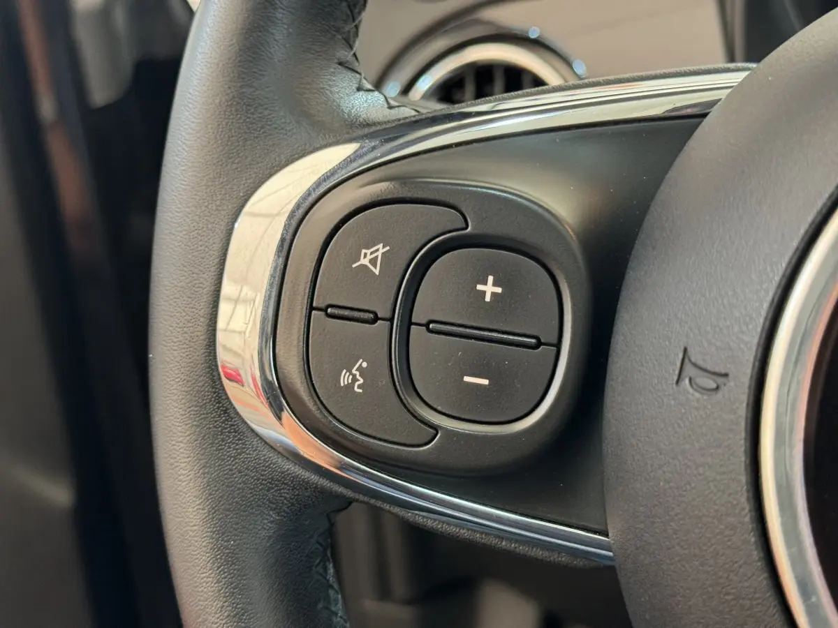 Gros plan sur les commandes audio au volant cuir d'une Fiat 500 noire, mettant en valeur les boutons de volume et de coupure du son.