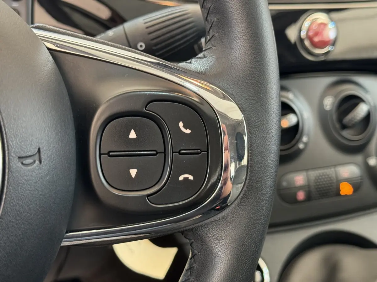 Gros plan sur les commandes du volant cuir noir de la Fiat 500 Lounge 2019 avec tableau de bord en arrière-plan.