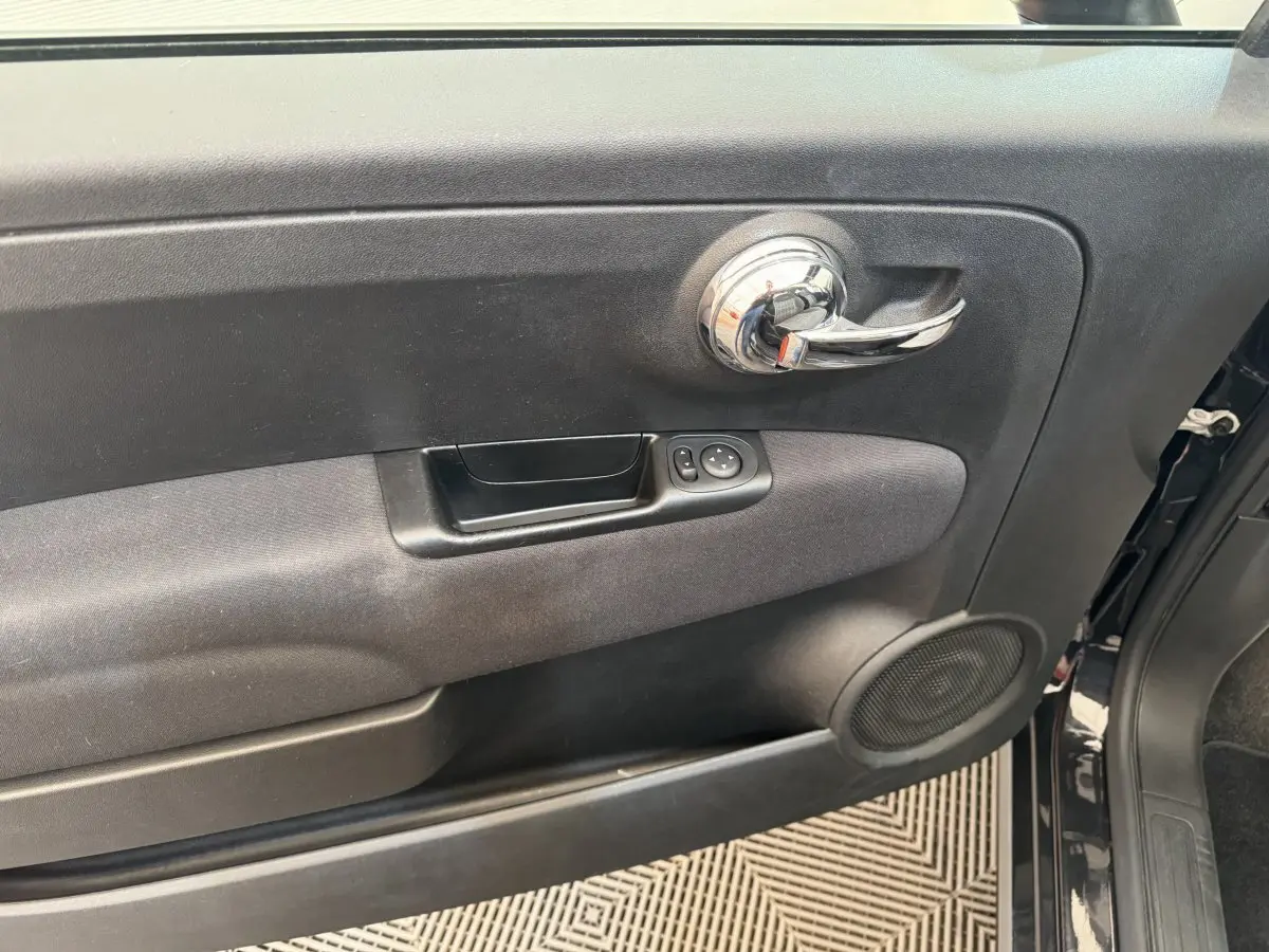 Gros plan sur la porte intérieure côté conducteur noire d'une FIAT 500 Lounge 2019 avec poignée chromée et commandes électriques.