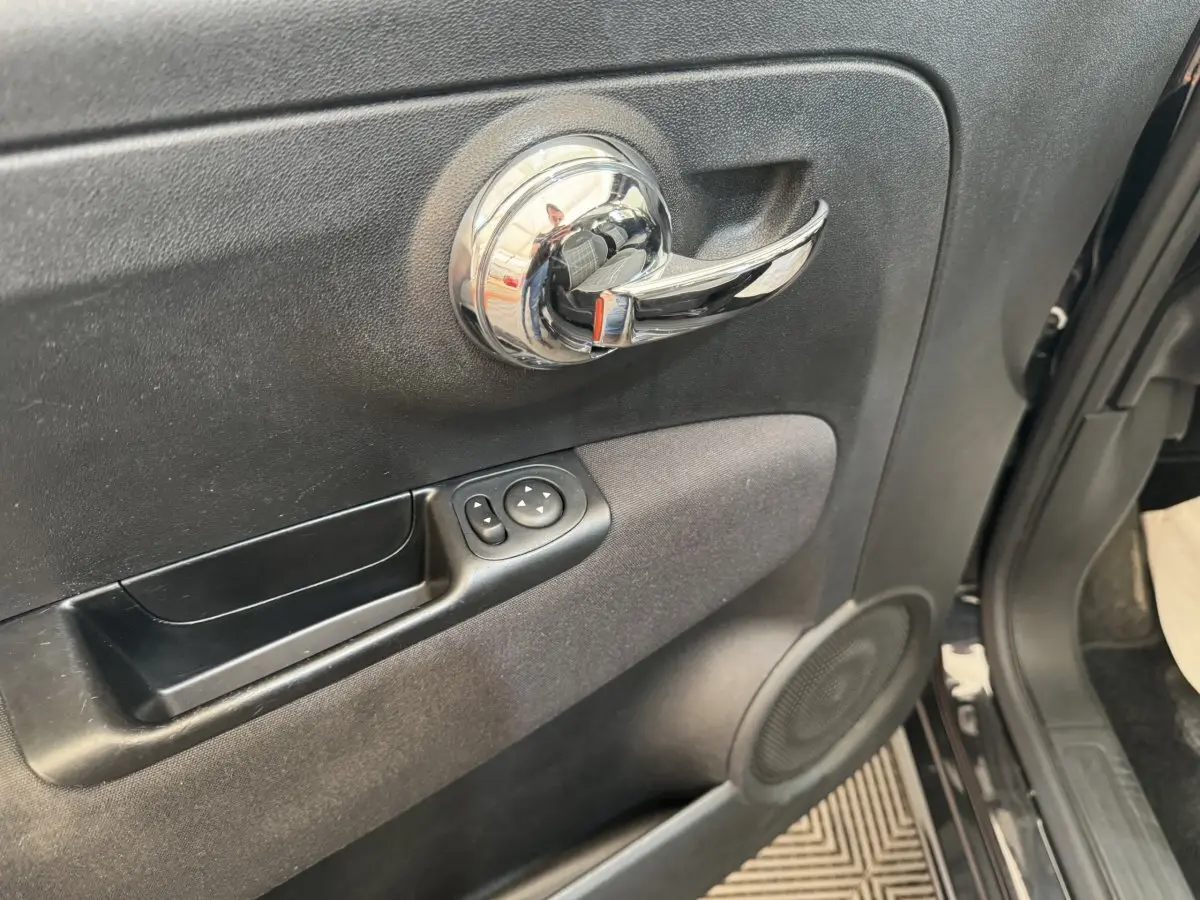 Gros plan sur la poignée intérieure chromée et les commandes de rétroviseurs du côté gauche d'une FIAT 500 noire de 2019.