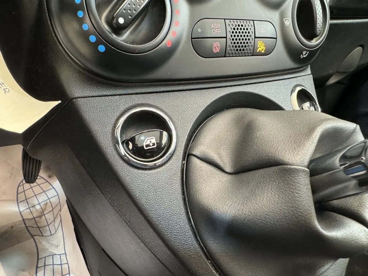 Gros plan sur la console centrale noire de la Fiat 500 Lounge 2019, montrant la commande de lève-vitre et le soufflet de levier de vitesses.