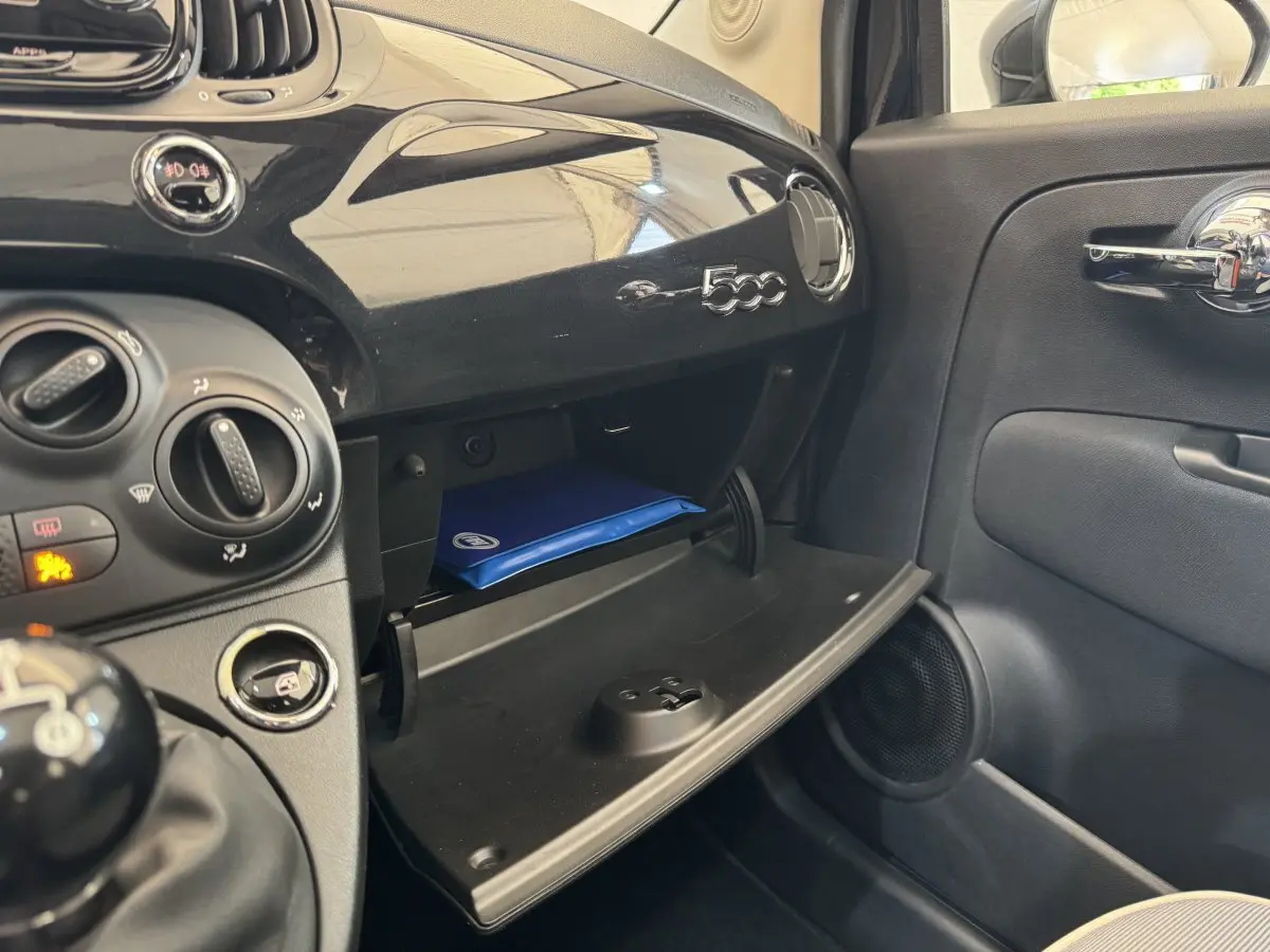 Intérieur de la FIAT 500 noire, vue côté passager sur la boîte à gants ouverte avec manuel bleu visible.