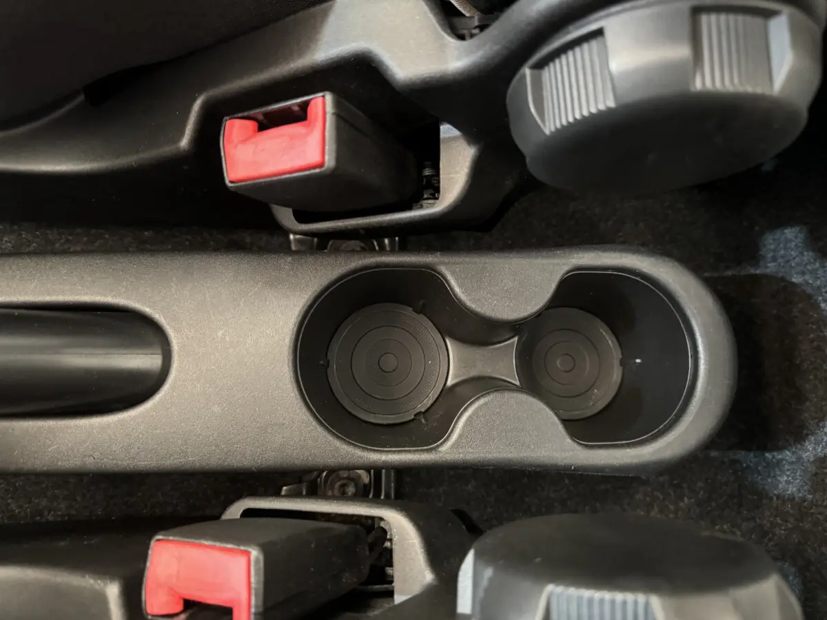 Gros plan sur les porte-gobelets noirs et les leviers de frein à main avec boutons rouges dans une Fiat 500 Lounge noire de 2019.