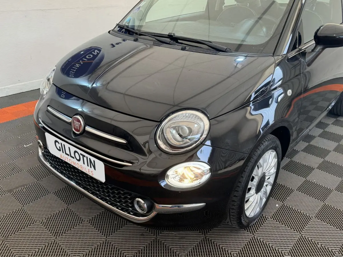 Vue 3/4 avant droite d'une FIAT 500 noire avec phares allumés et jantes argentées sur sol damier.
