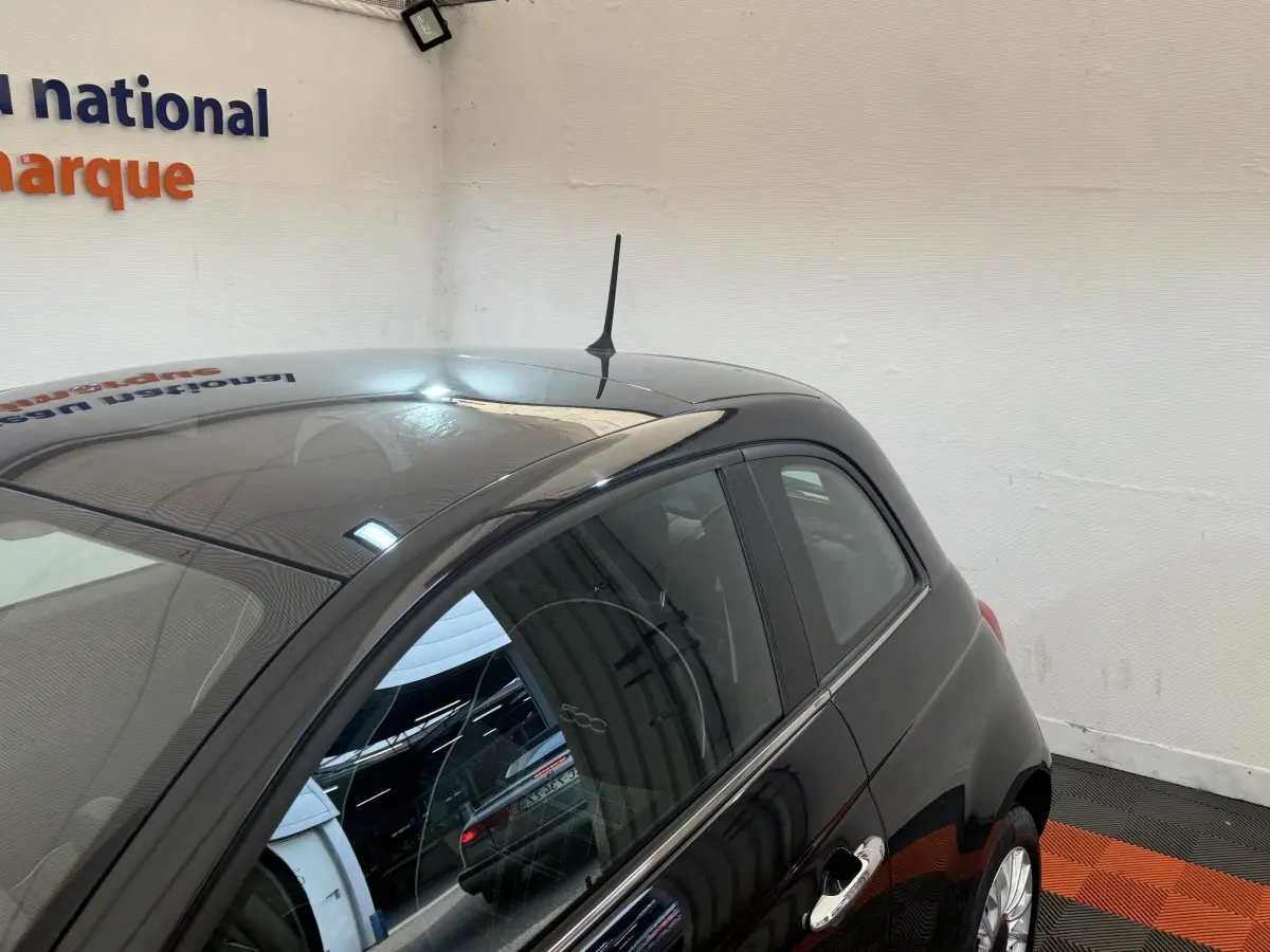 Vue 3/4 arrière droite d'une Fiat 500 noire brillante avec antenne de toit et poignées chromées visibles.