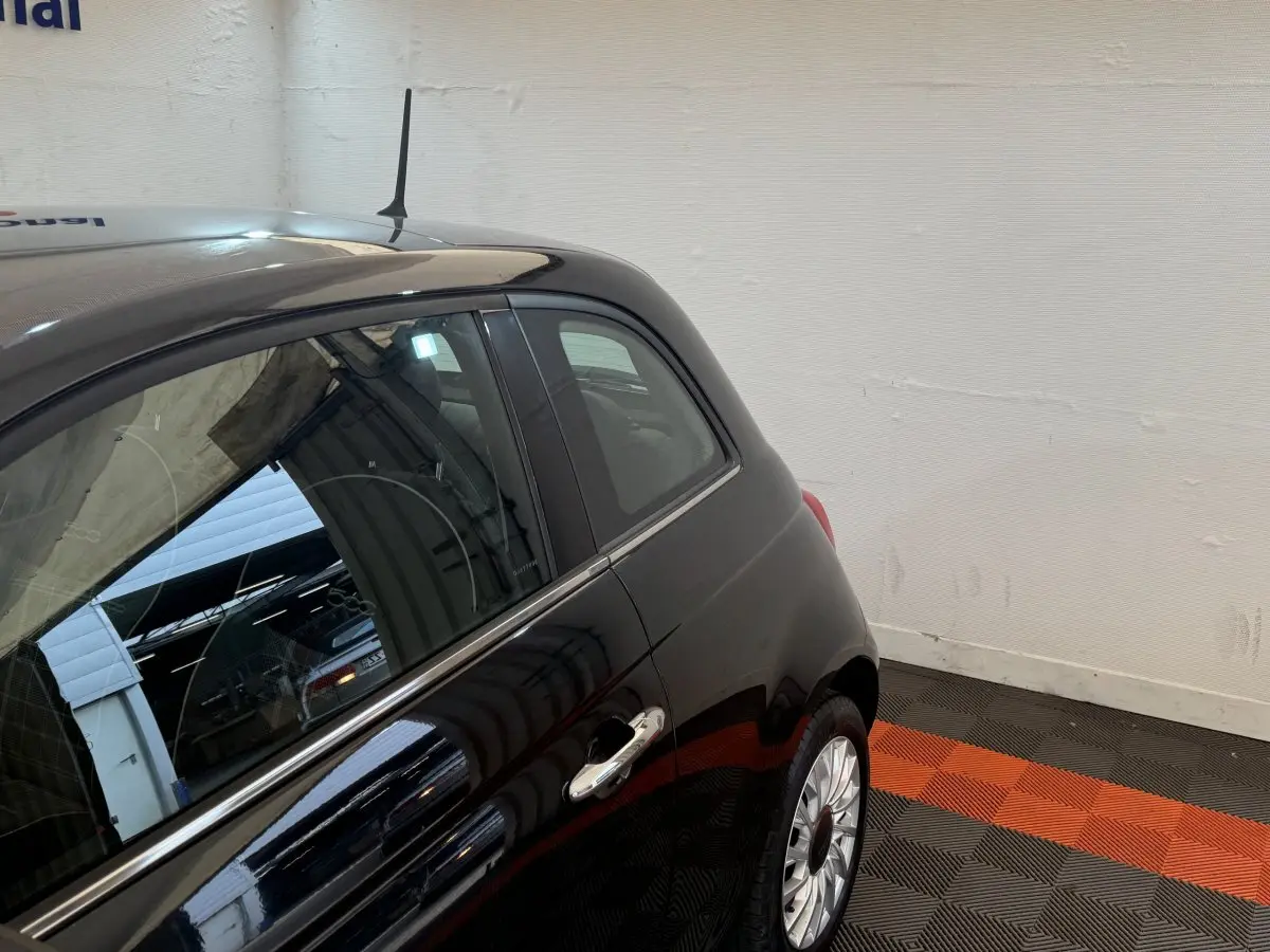 Vue côté droit arrière d'une FIAT 500 noire brillante avec jante argentée dans un garage intérieur.