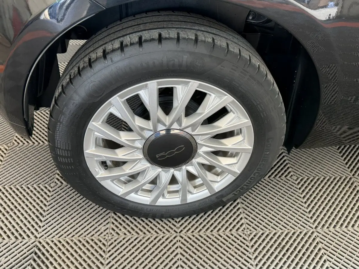 Gros plan sur la roue avant gauche noire d'une Fiat 500 1.2 8V 69ch Lounge avec jante argentée à rayons fins.