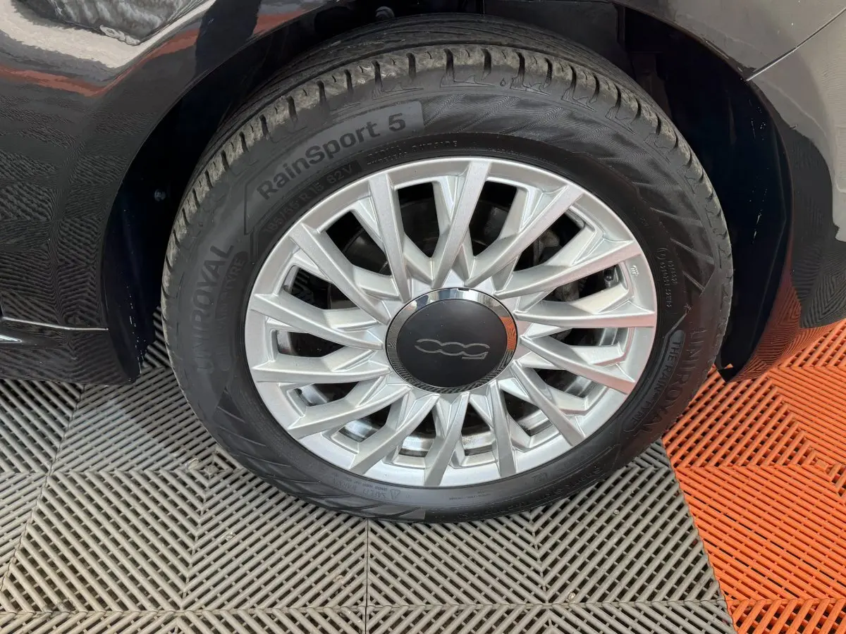 Gros plan sur la roue avant droite noire d'une FIAT 500 1.2 8V 69ch Lounge avec jante argentée à rayons fins