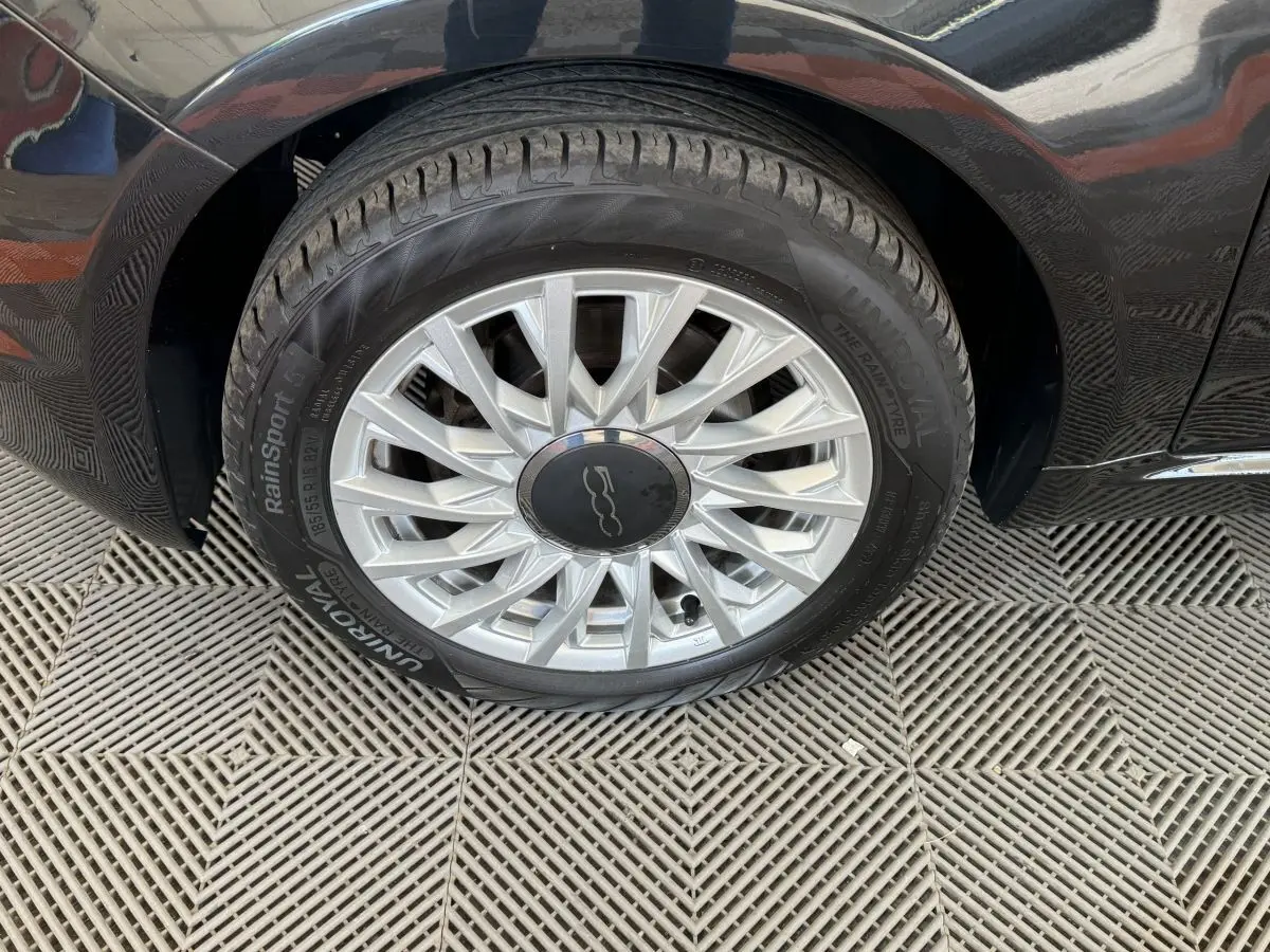 Gros plan sur la roue avant droite noire d'une FIAT 500 Lounge 2019 avec jante argentée au design étoilé.