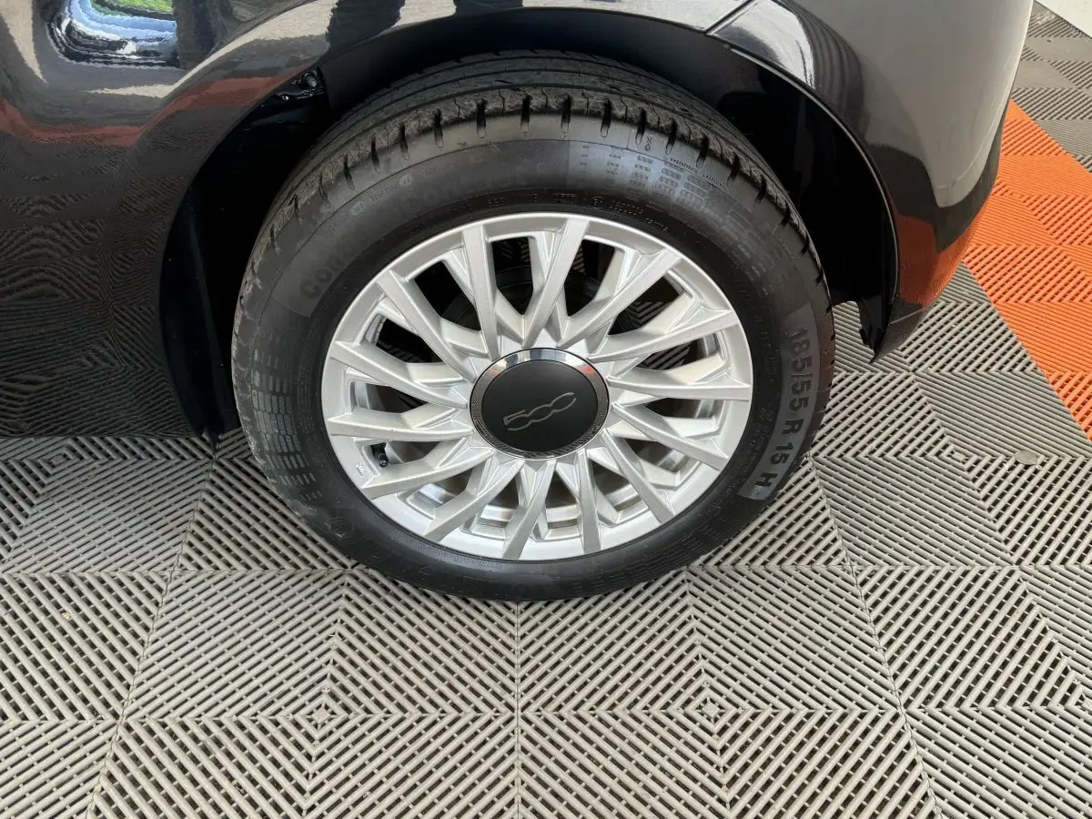 Gros plan sur la roue avant droite noire d'une FIAT 500 1.2 8V 69ch Lounge avec jante argentée à rayons fins.