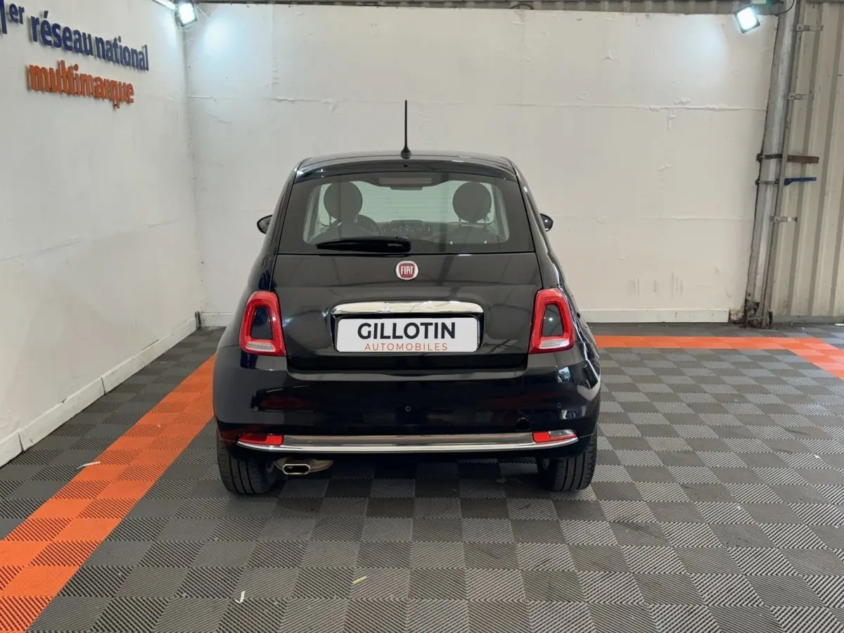 Vue arrière d'une FIAT 500 noire stationnée en intérieur sur un sol à damiers gris et orange.