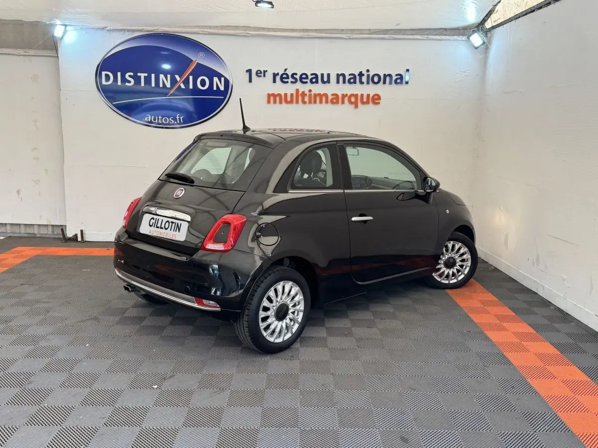 Vue 3/4 arrière droite d'une Fiat 500 noire 2019 dans un showroom avec jantes argentées et feux arrière LED.