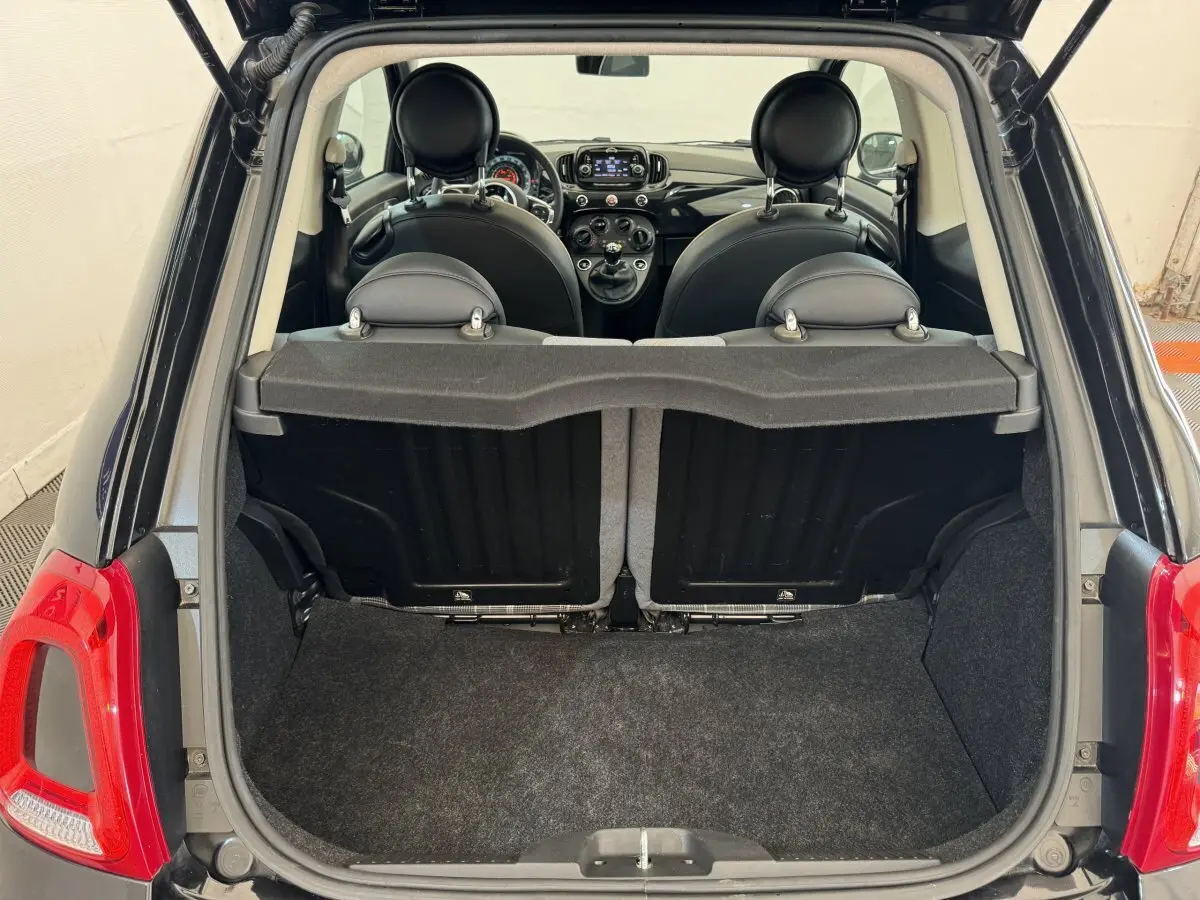 Vue arrière du coffre ouvert d'une FIAT 500 noire montrant l'intérieur et les sièges avant en cuir noir.