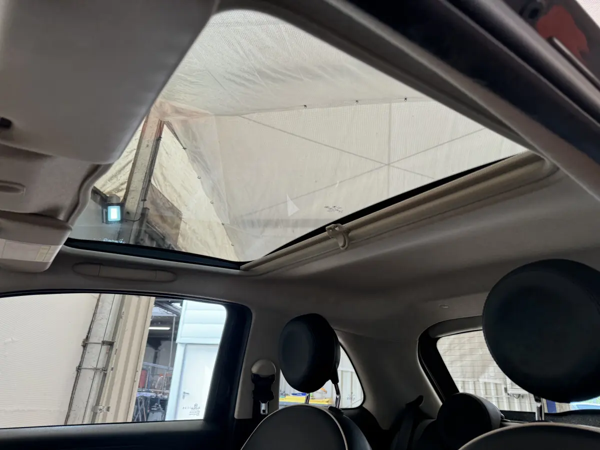 Toit panoramique ouvert vu de l'intérieur arrière droit de la Fiat 500 noire avec sièges avant ronds.
