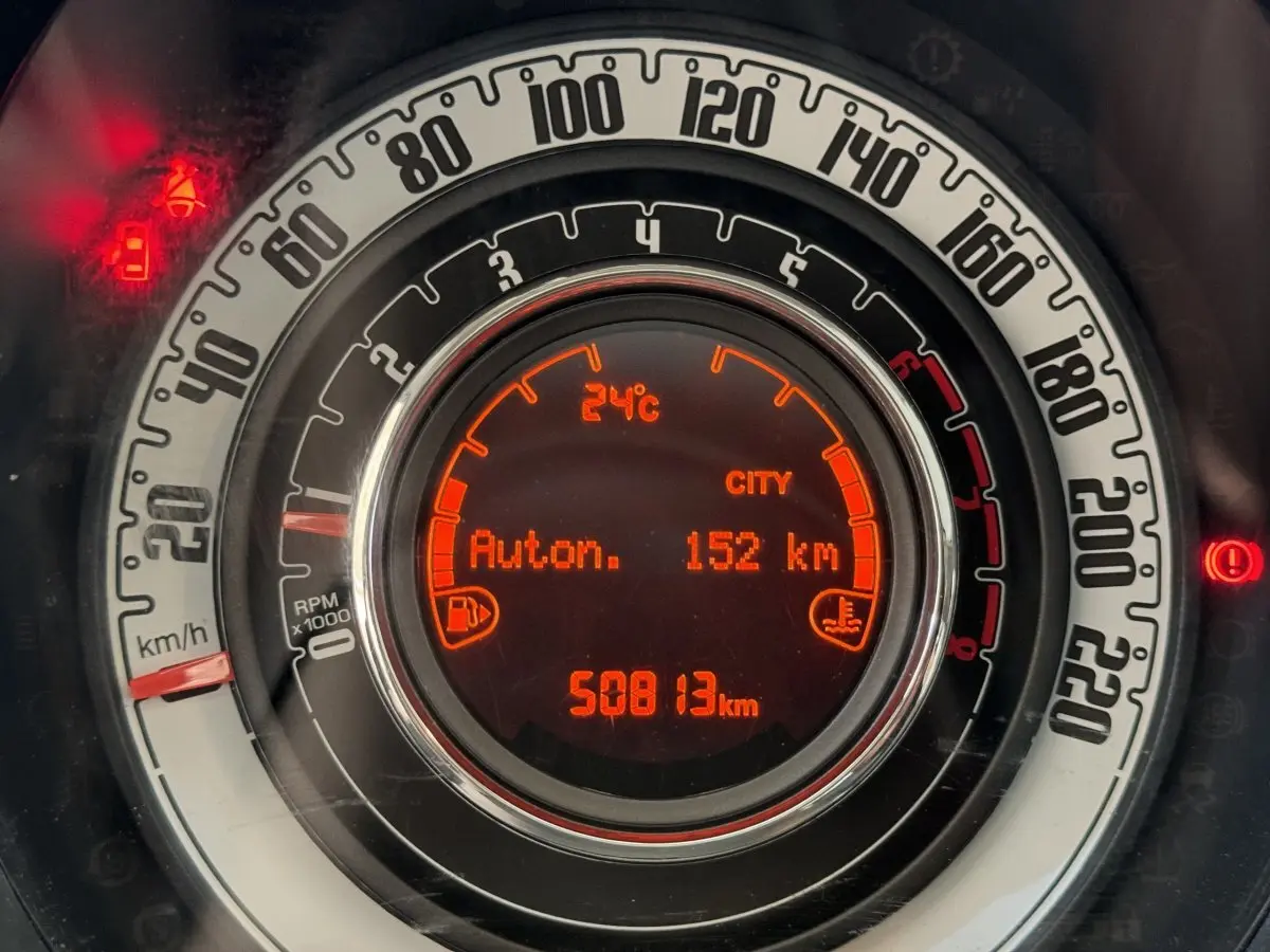 Gros plan sur le tableau de bord numérique orange d'une Fiat 500 noire, affichant la vitesse et l'autonomie.