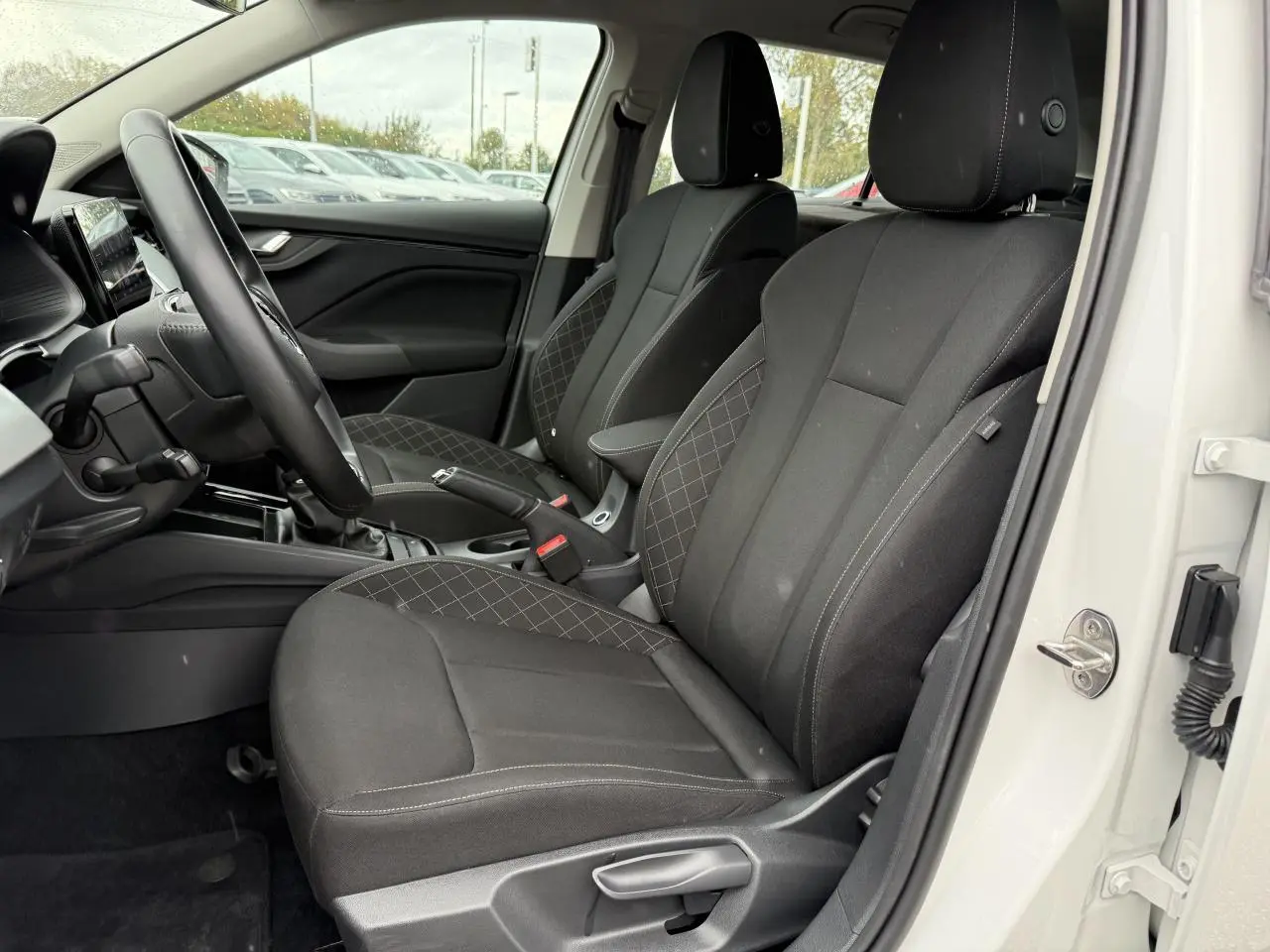 Vue intérieure côté conducteur d'une Skoda Scala blanche 2023, sièges noirs avec surpiqûres et console centrale visible.