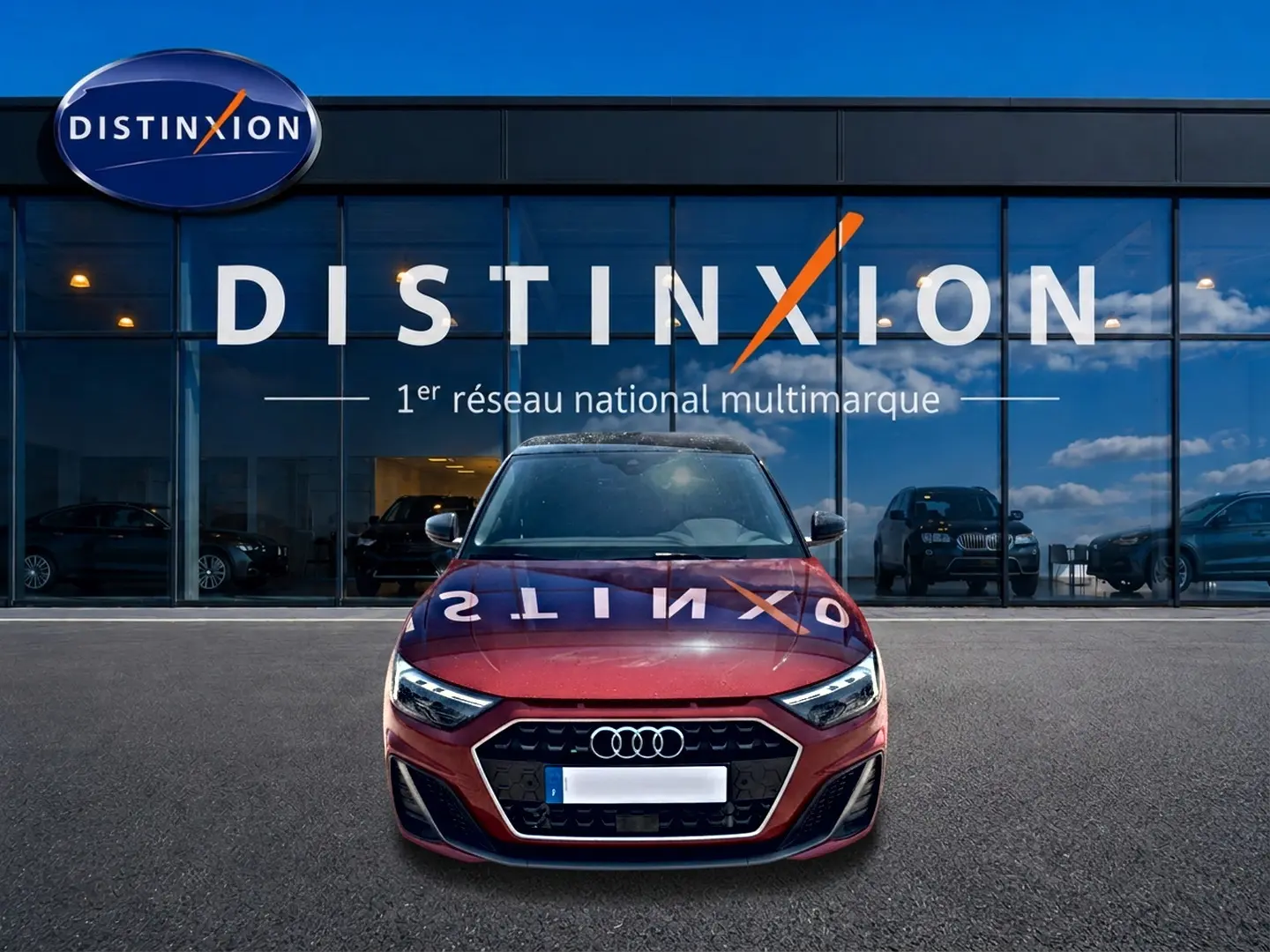 Audi A1 Sportback rouge et noir vue de face, avec calandre hexagonale et phares LED devant un showroom Distinxion.