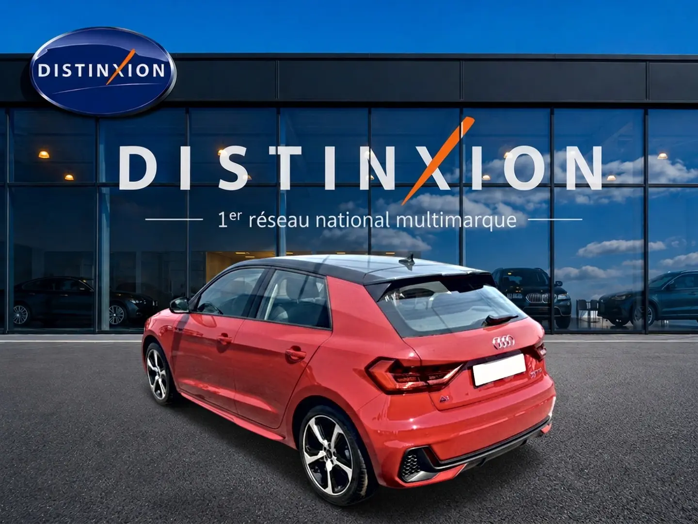 Audi A1 Sportback rouge et noir vue 3/4 arrière droit, avec jantes alu et becquet arrière visible devant une vitrine Distinxion.