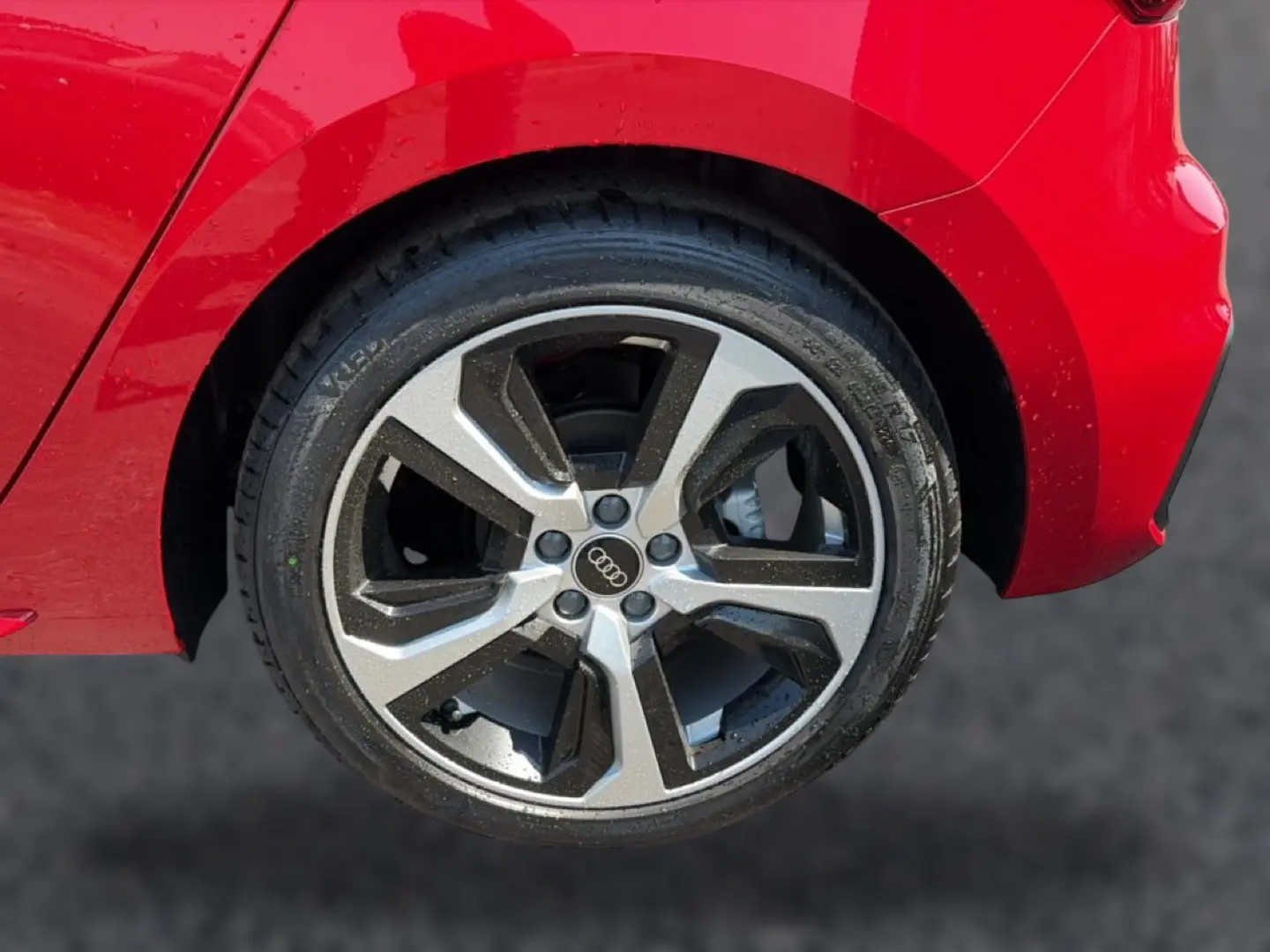 Gros plan sur la roue arrière droite d’une Audi A1 Sportback rouge avec jante alu bicolore et logo Audi au centre.
