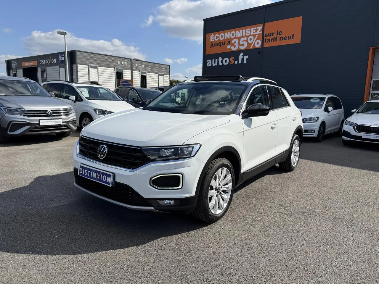 Volkswagen T-Roc blanc en 3/4 avant droit, avec toit ouvrant et jantes alliage visibles, sur parking extérieur.