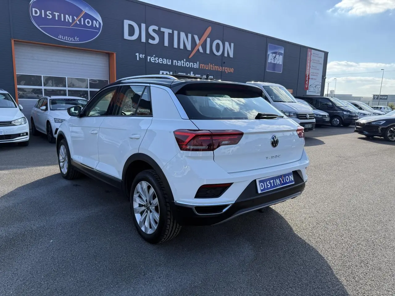 Volkswagen T-Roc blanc vue 3/4 arrière droit, avec toit noir et feux arrière LED distinctifs.