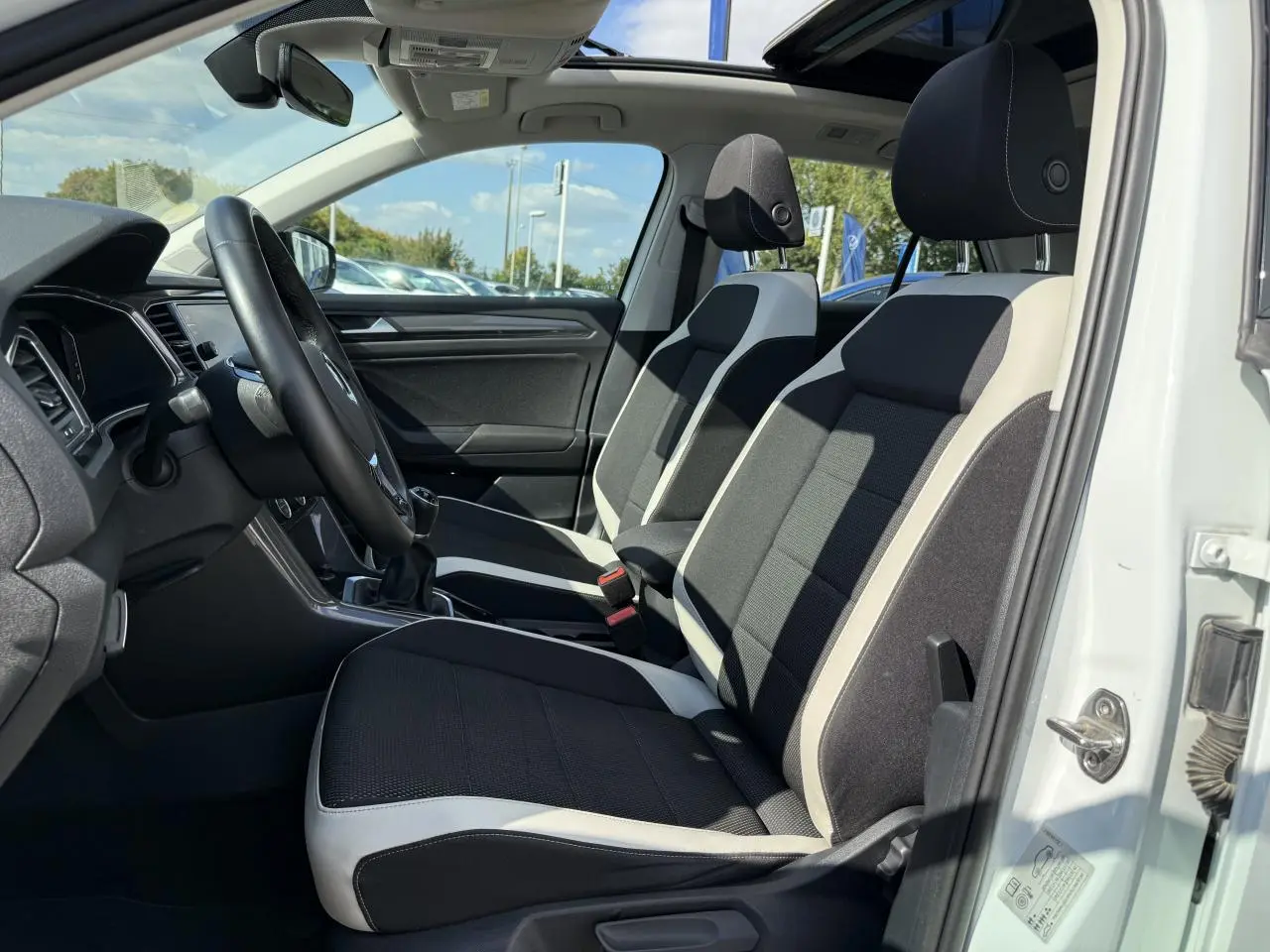 Vue intérieure côté gauche du Volkswagen T-Roc blanc 2022, montrant les sièges avant bicolores et le volant multifonction.