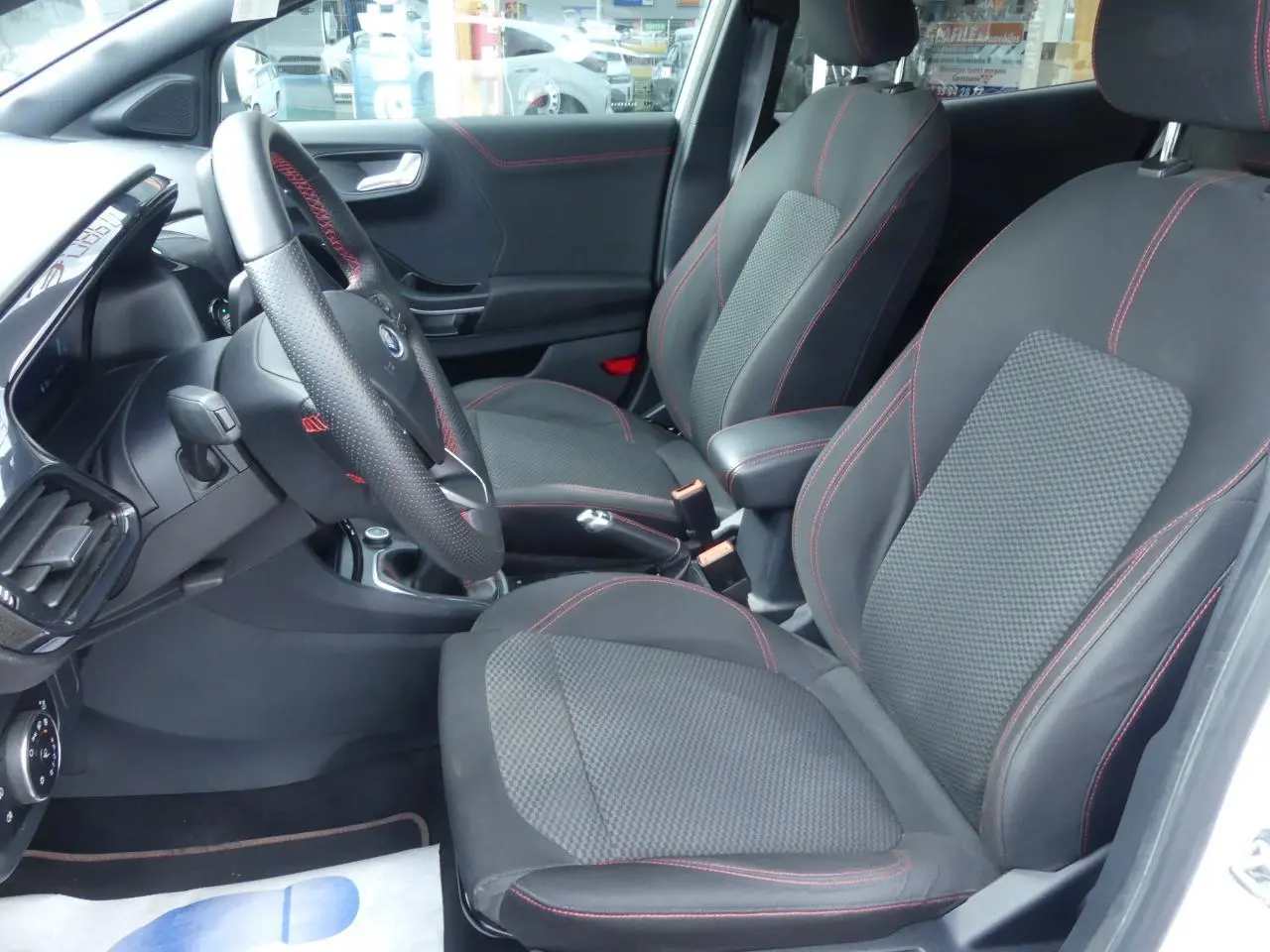 Intérieur avant droit du Ford Puma blanc 2020 ST Line, sièges tissu noir avec surpiqûres rouges et volant méplat.