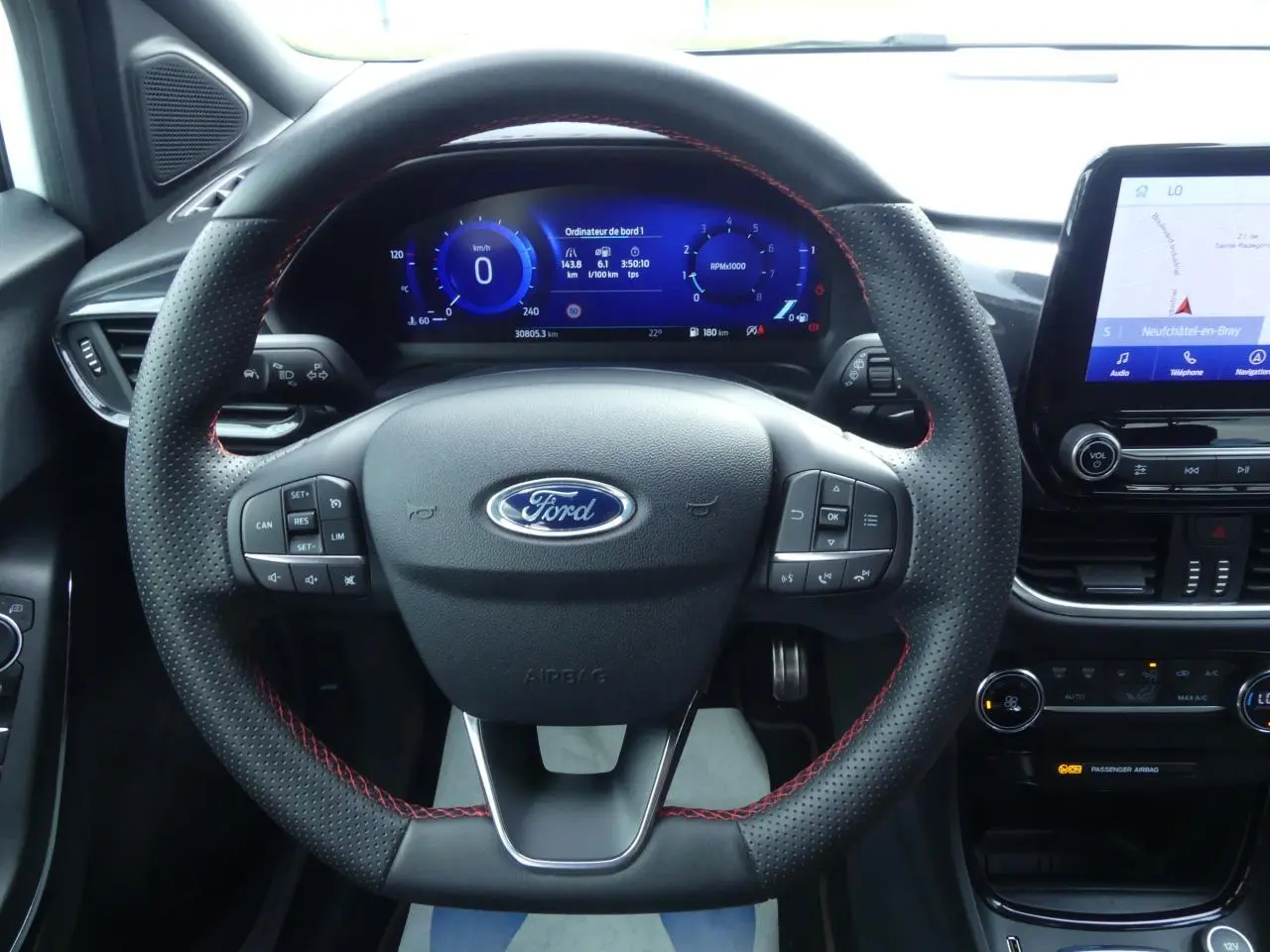 Vue intérieure centrée sur le volant perforé noir avec surpiqûres rouges du Ford Puma 2020, tableau de bord numérique et écran tactile.