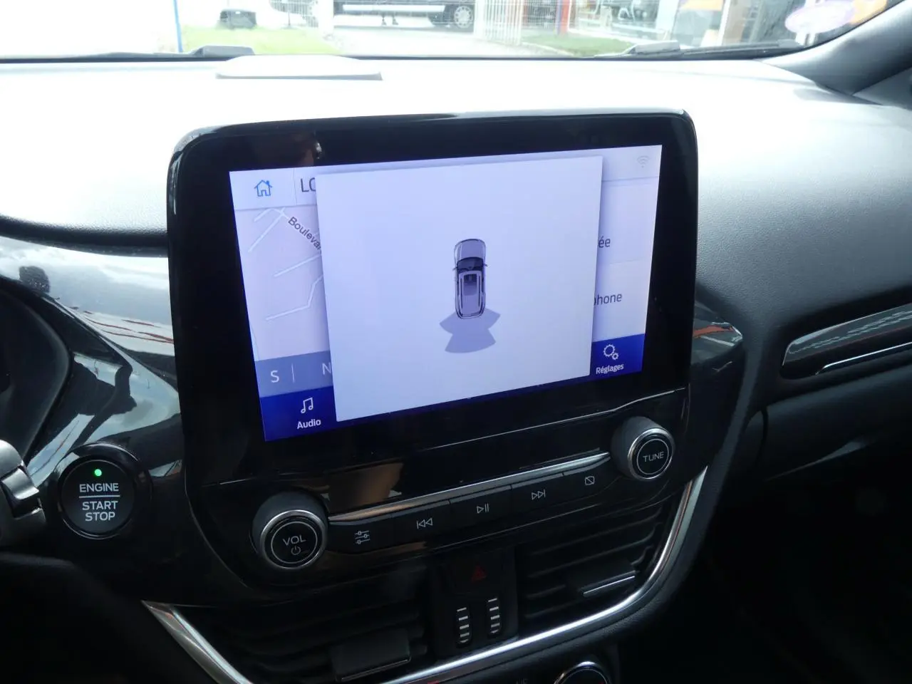 Vue rapprochée de la console centrale noire du Ford Puma 2020 avec écran tactile affichant une aide au stationnement.