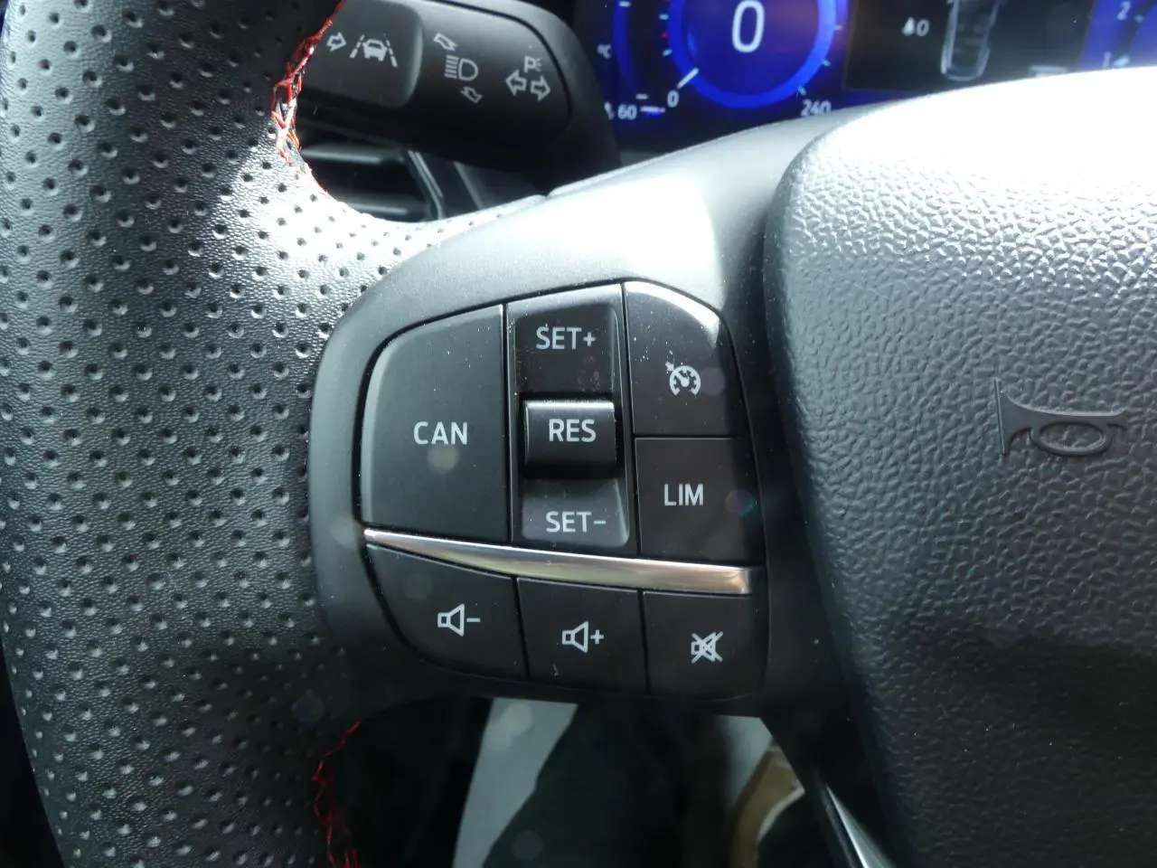 Gros plan sur les commandes de régulateur de vitesse et volume au volant perforé noir du Ford Puma blanc 2020.