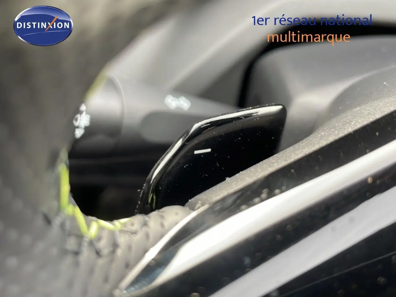 Gros plan sur la palette de changement de vitesse noire et brillante, volant perforé avec surpiqûres vertes, intérieur Peugeot 308 gris.