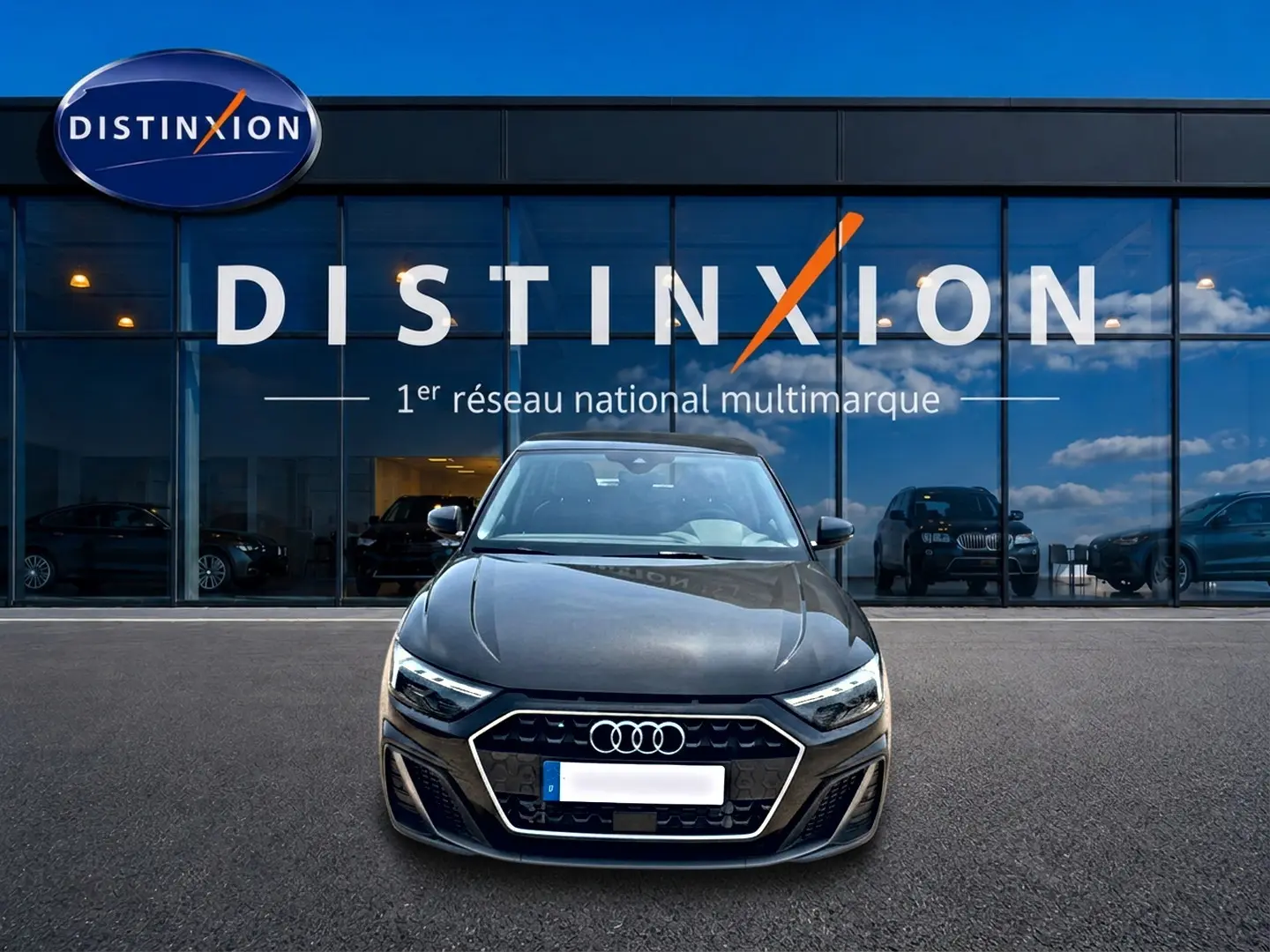 Audi A1 Sportback noir vue de face, mettant en valeur sa calandre hexagonale et ses phares LED devant un showroom Distinxion.
