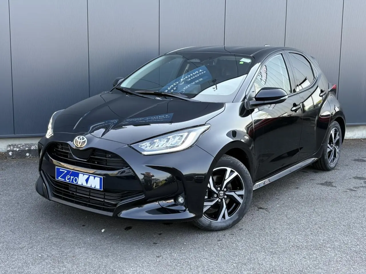 Toyota Yaris hybride noire vue en 3/4 avant droit avec jantes alliage et phares LED allumés.
