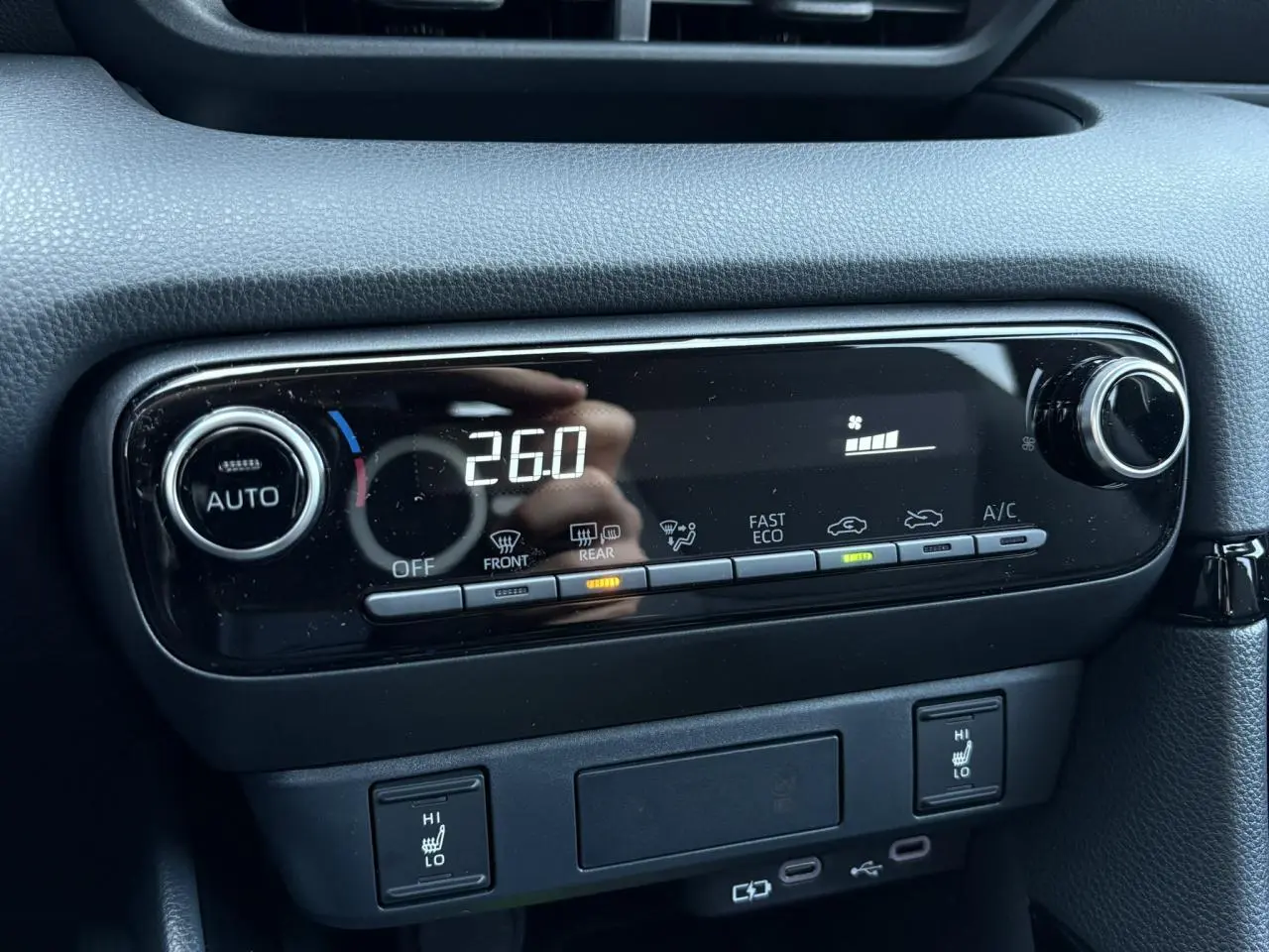 Vue rapprochée de la console centrale noire de la Toyota Yaris Hybride 2025 avec commandes climatisation et sièges chauffants.