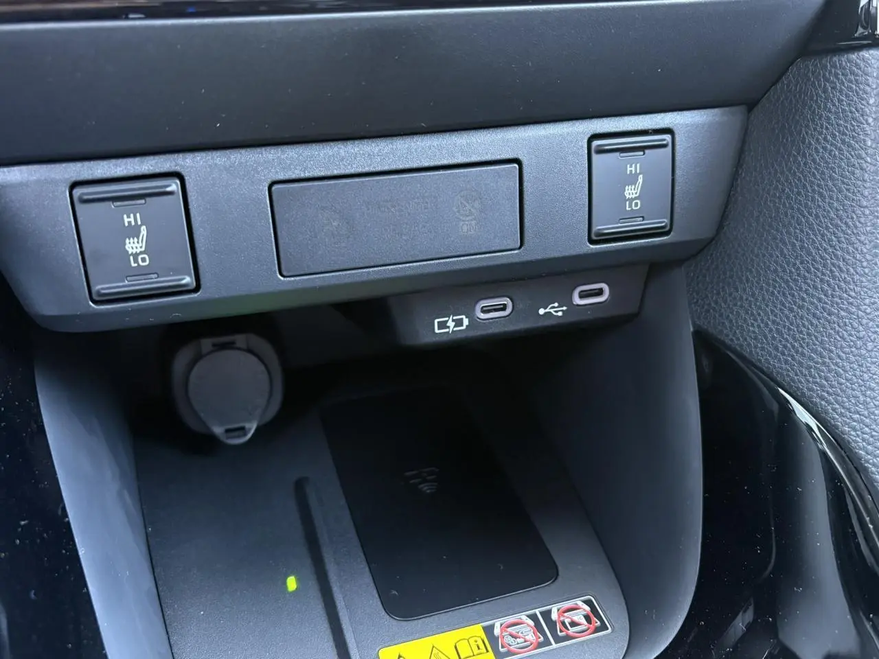 Vue rapprochée du chargeur à induction et des commandes des sièges chauffants sur la console centrale d'une Toyota Yaris noire.