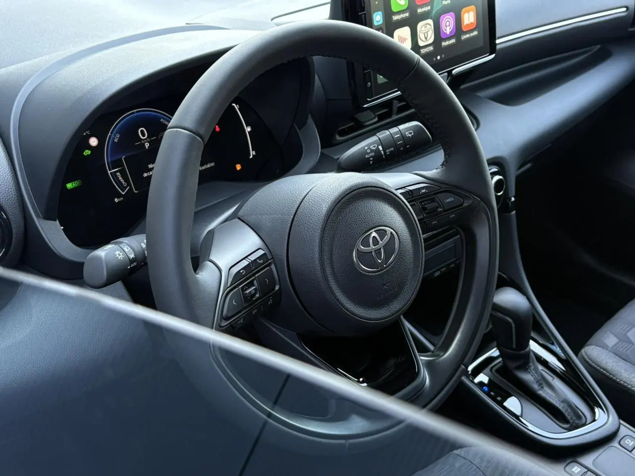 Intérieur de la Toyota Yaris hybride 2025 vu côté conducteur, volant cuir noir et tableau de bord numérique.