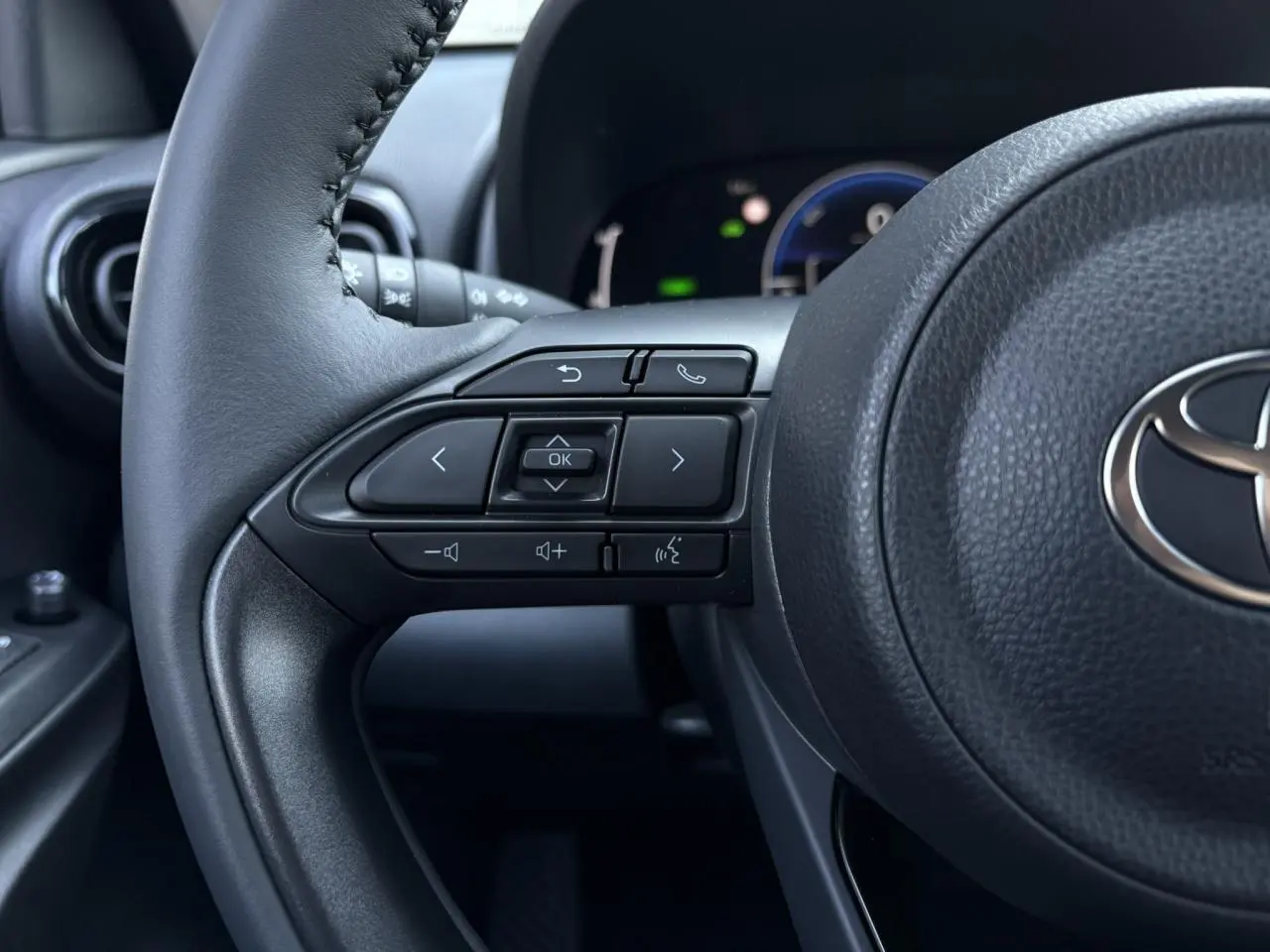 Gros plan sur le volant cuir noir de la Toyota Yaris 2025, avec commandes multifonctions et logo Toyota visible au centre.