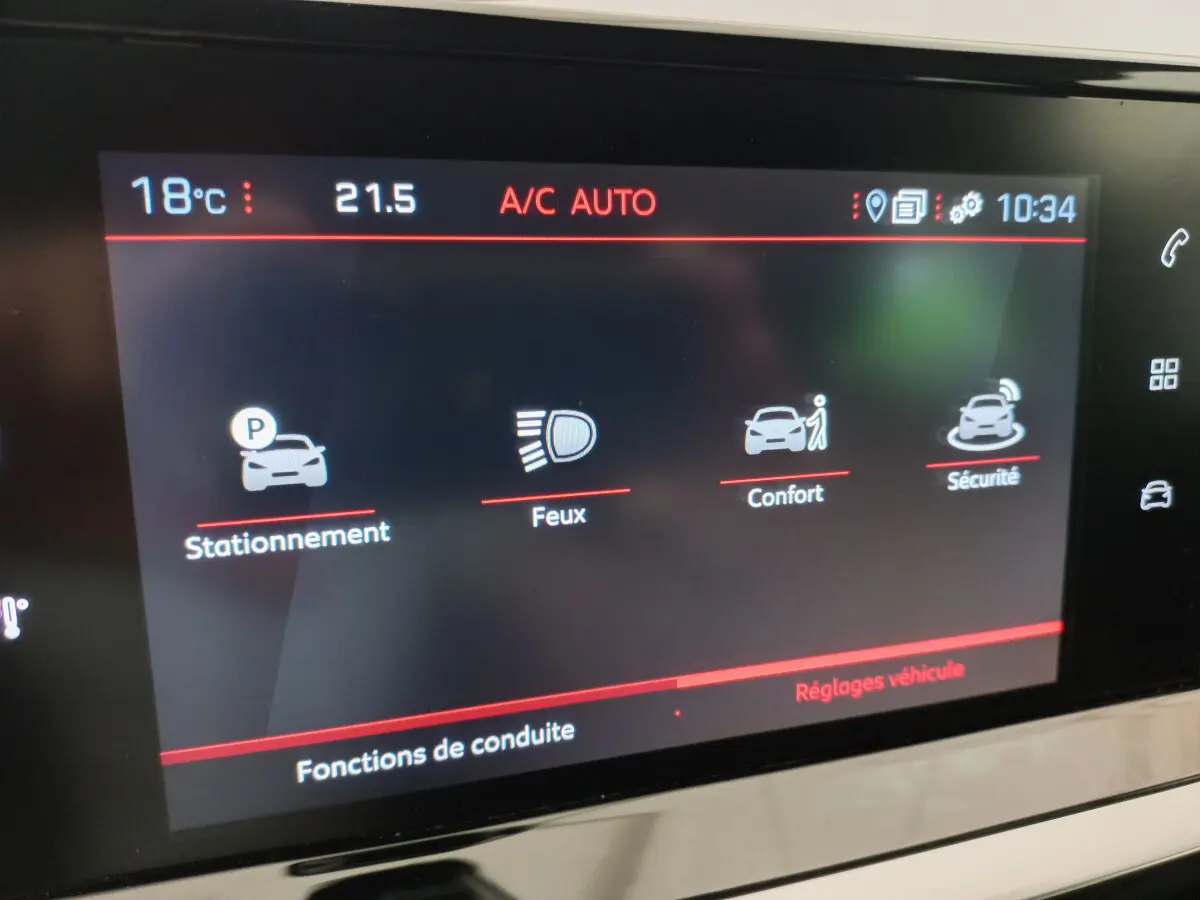 Écran tactile intérieur du tableau de bord de la Peugeot 208 blanc, affichant les réglages de conduite stationnement, feux, confort et sécurité.