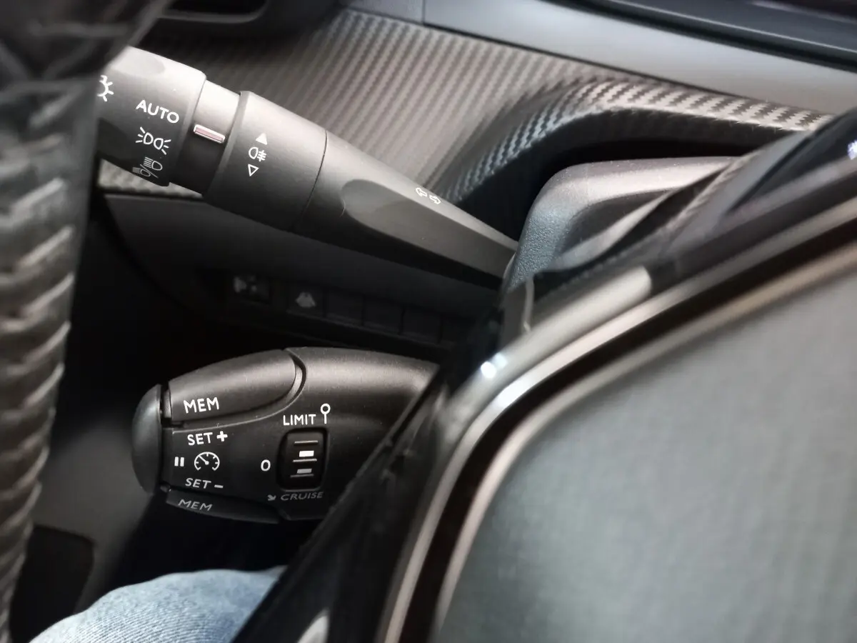 Gros plan sur les commandes du régulateur de vitesse et des feux dans l'habitacle d'une Peugeot 208 blanche.