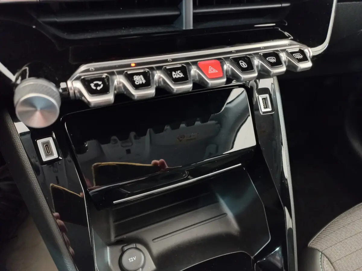 Gros plan sur la console centrale noire brillante de la Peugeot 208 PureTech 100 S&S Allure avec boutons de commande et ports USB visibles