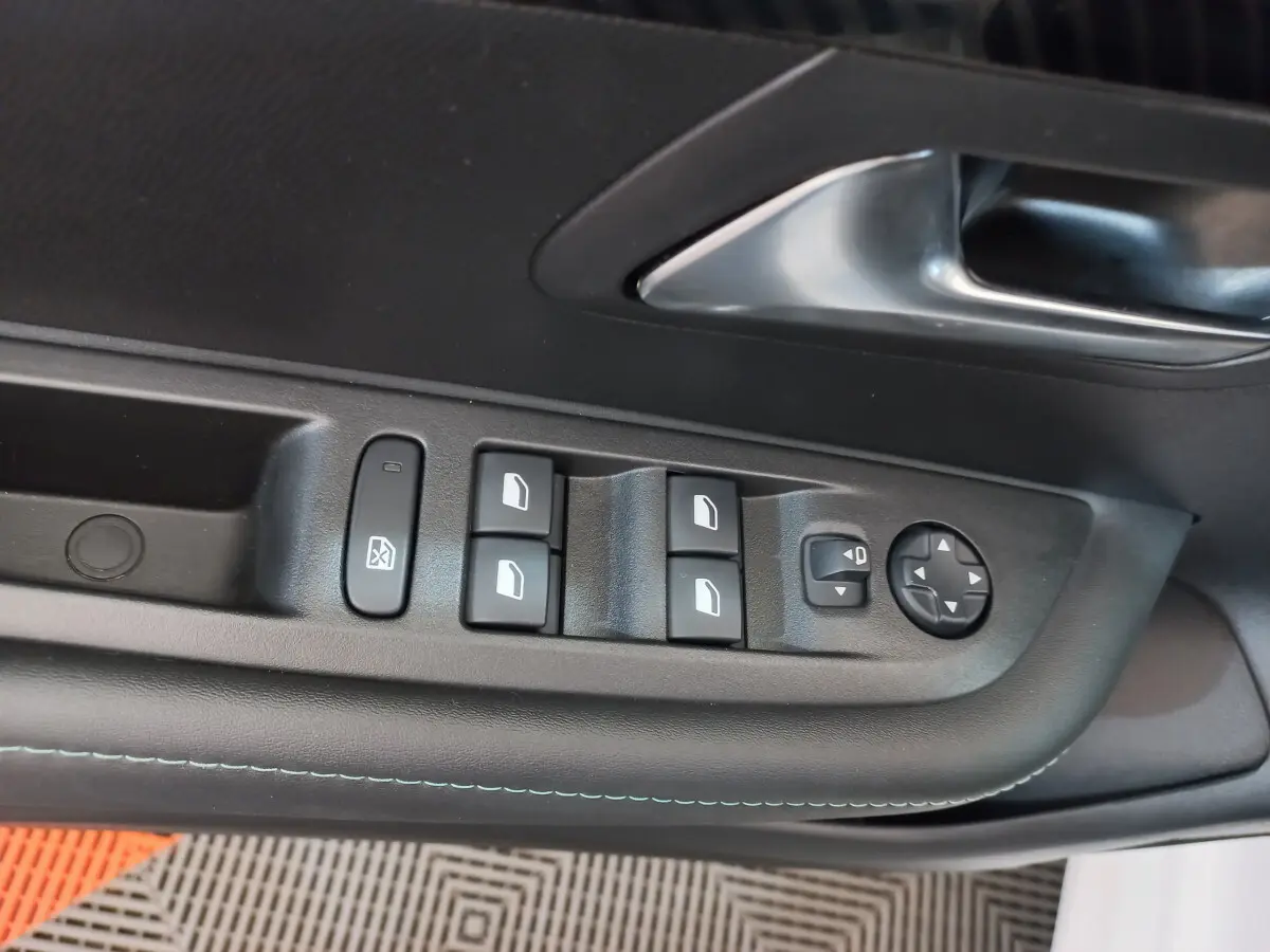 Gros plan sur la commande des vitres et rétroviseurs côté conducteur d'une Peugeot 208 blanche, intérieur noir.